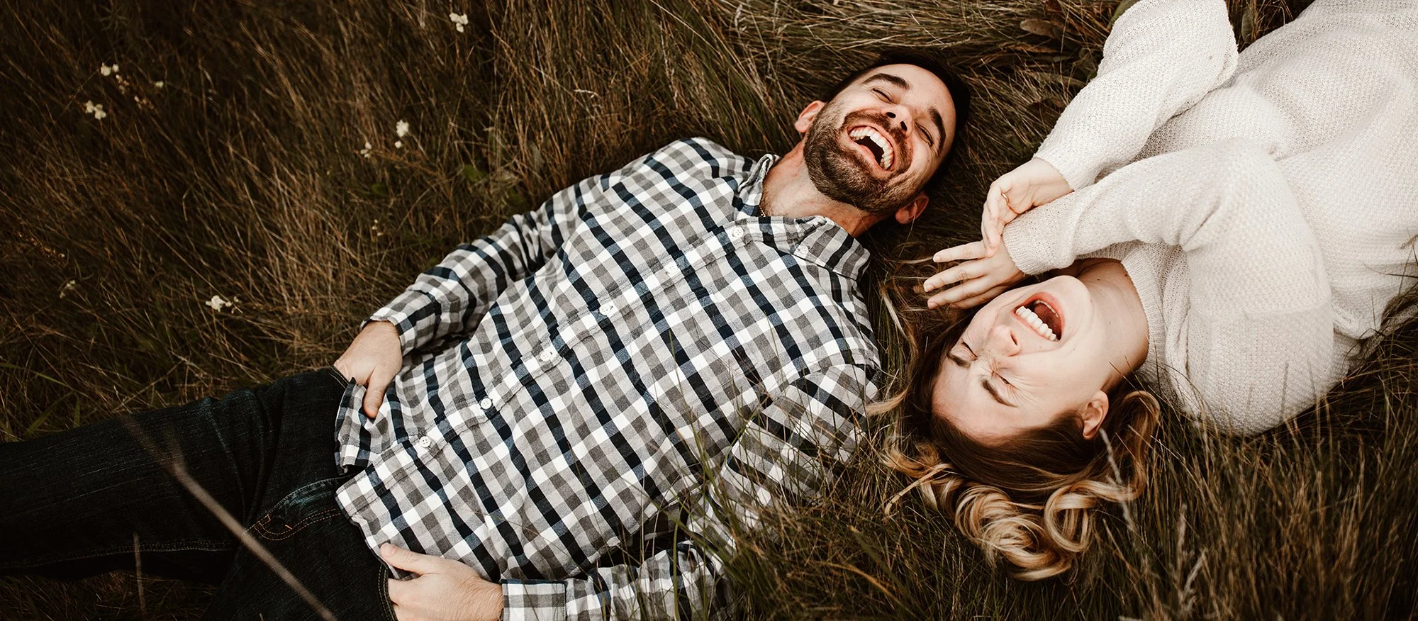engagement session couple laying in tall grass and laughing hysterically
