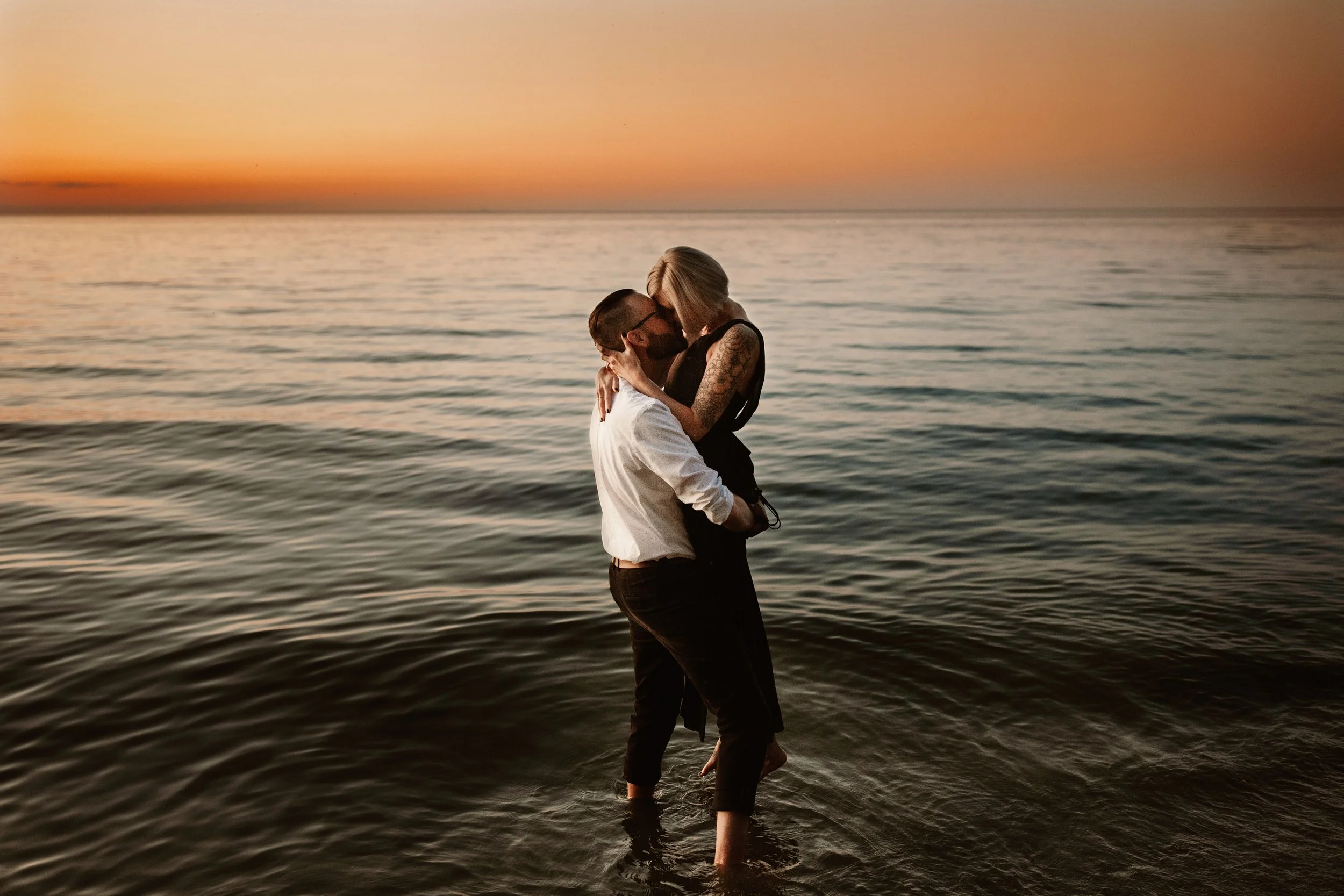 man hoisting woman up in the lake at sunset for a kiss 