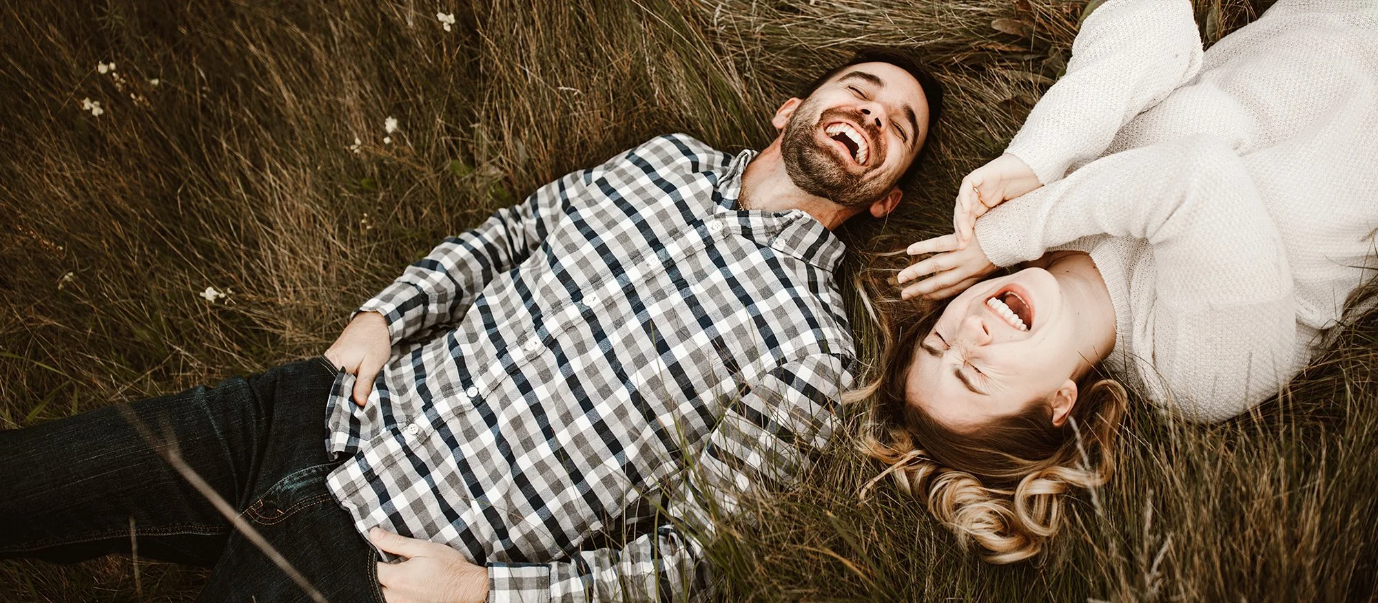 engagement session couple laying in tall grass and laughing hysterically