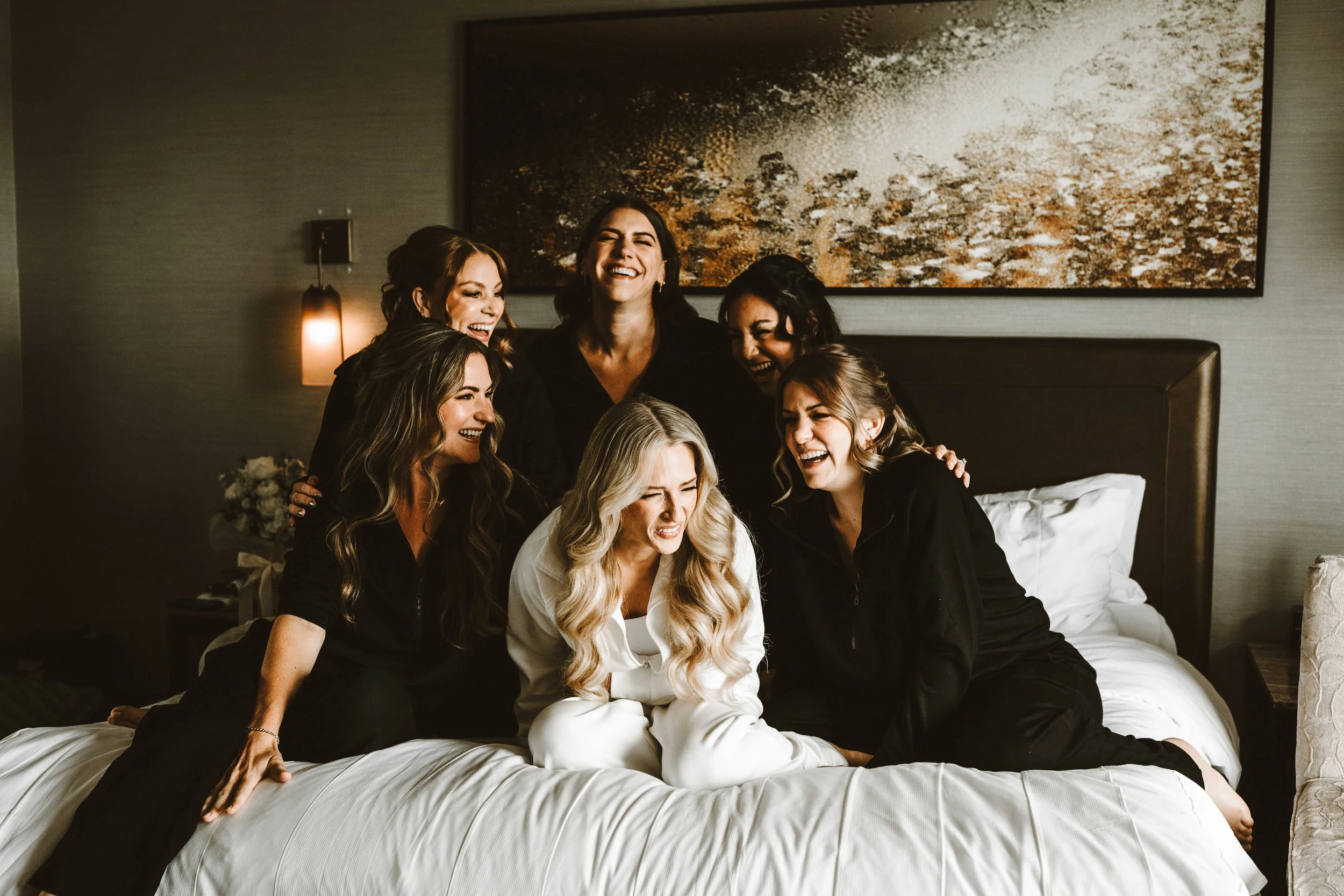 bride with her bridesmaids laughing on the hotel bed