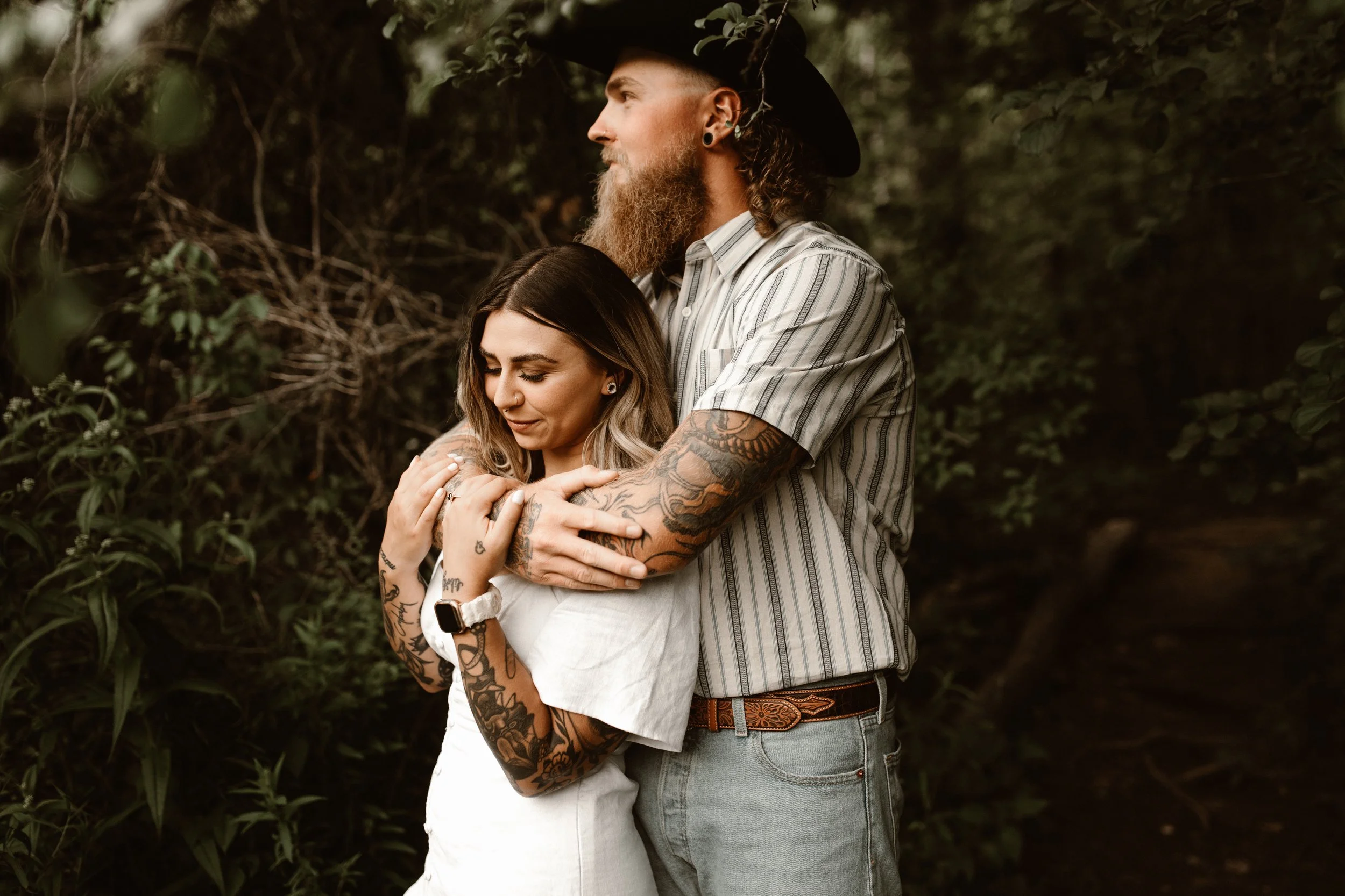 tattooed cowboy embracing his girl in the woods
