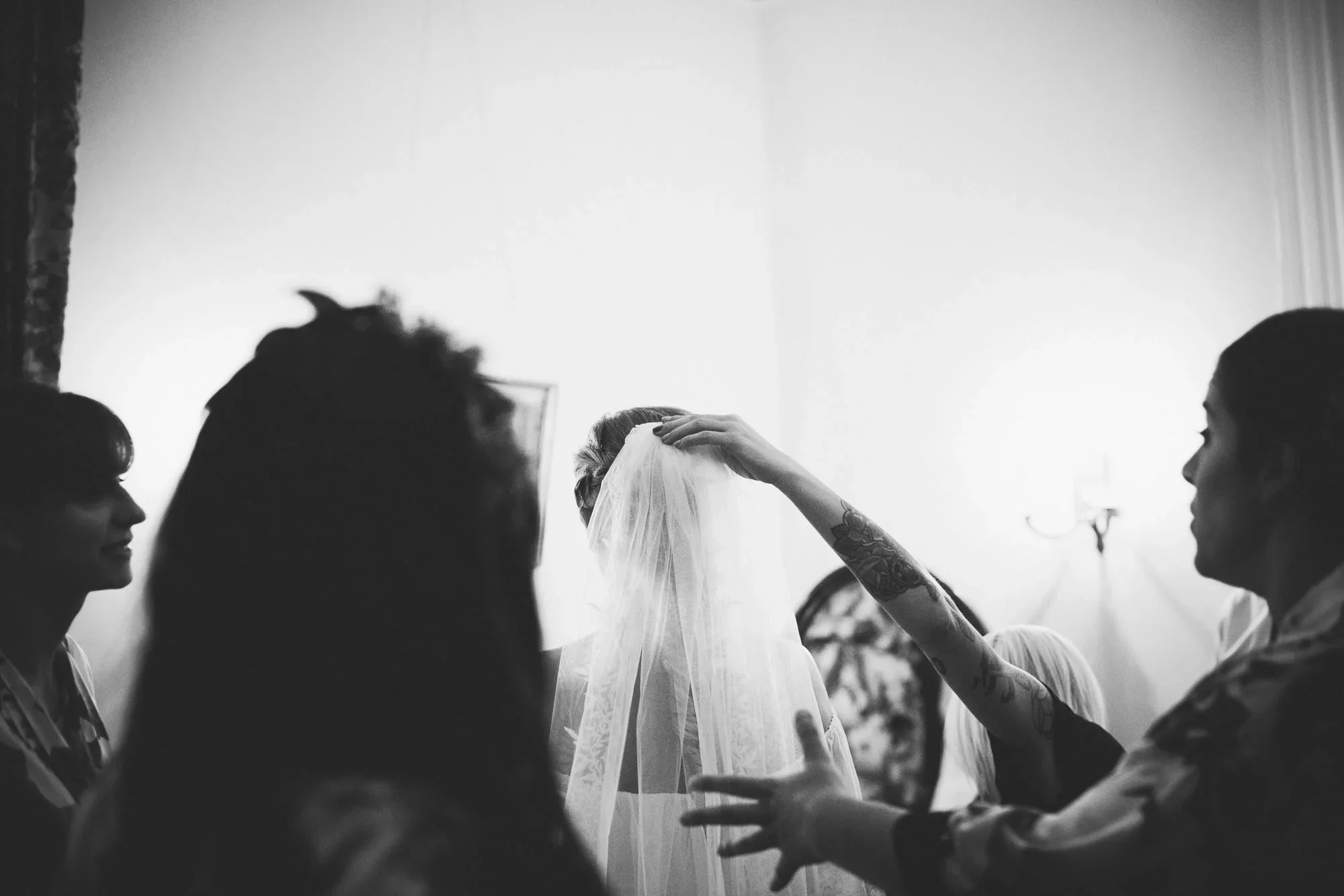 back and white image of bridesmaids placing veil on bride