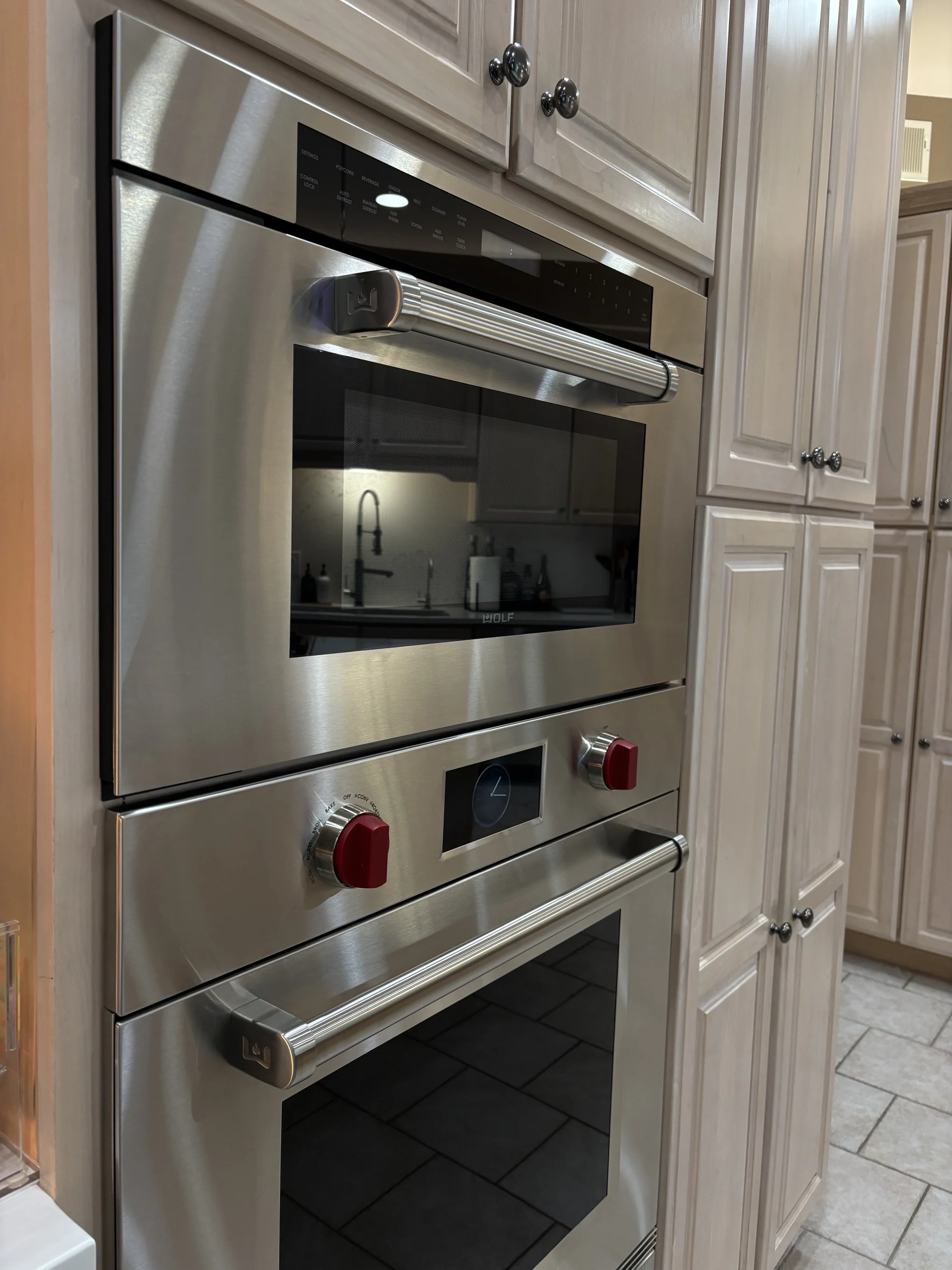 Stainless steel Wolf built-in double wall oven with red knobs, displayed among white kitchen cabinets.