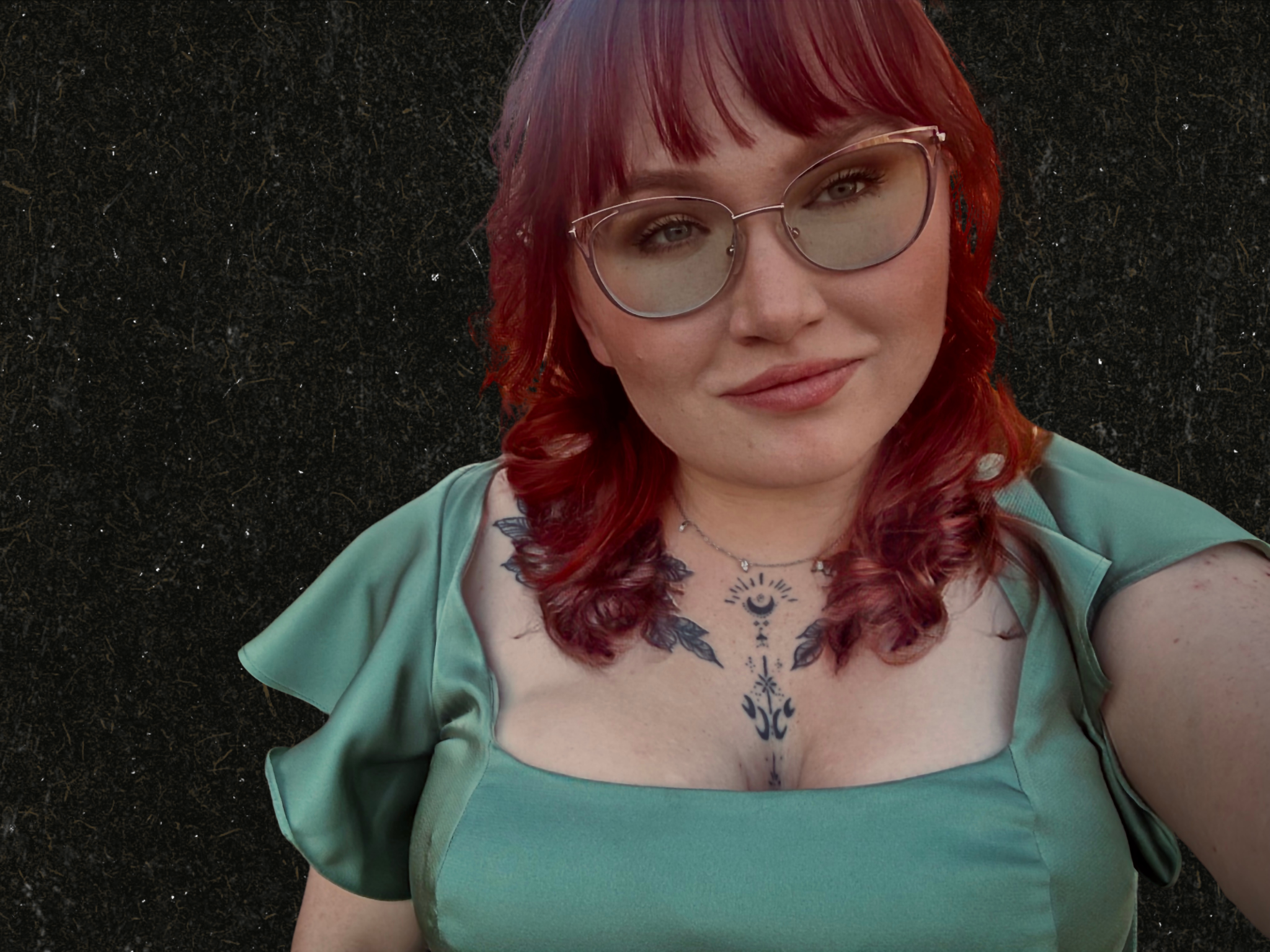 Portrait of Blair Briar, dark romance author, with red hair, oversized glasses, and a mint-green dress against a dark textured background.