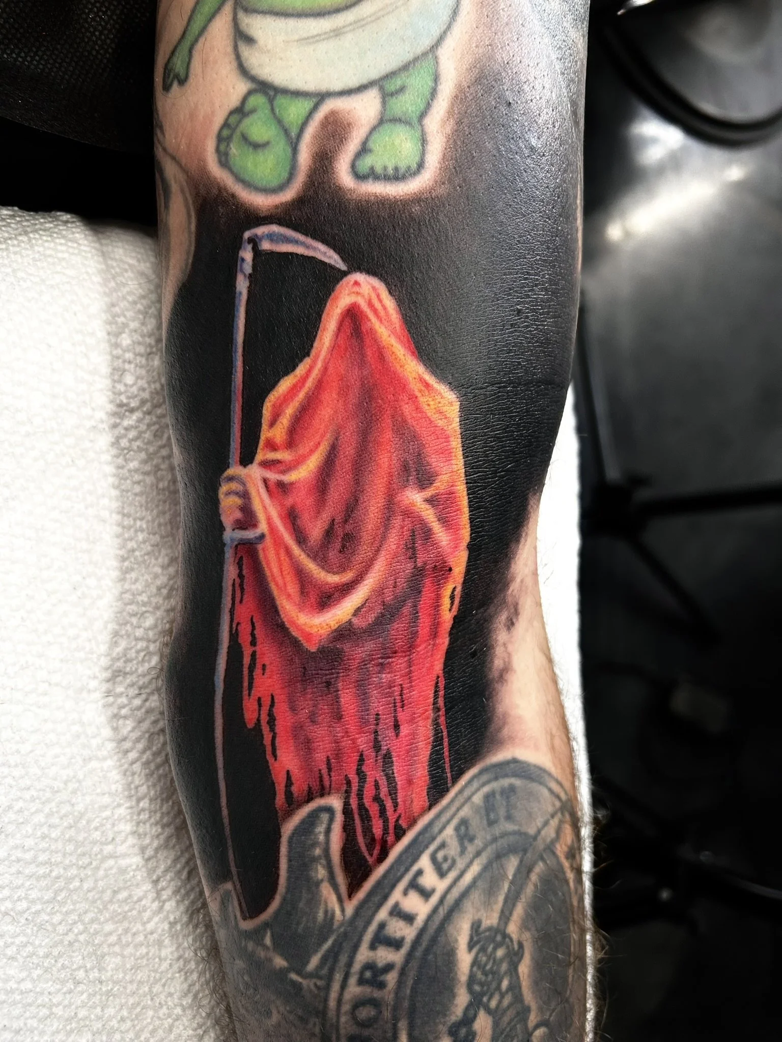 Close-up of a colorful tattoo featuring a red-orange winged creature on a person's leg.
