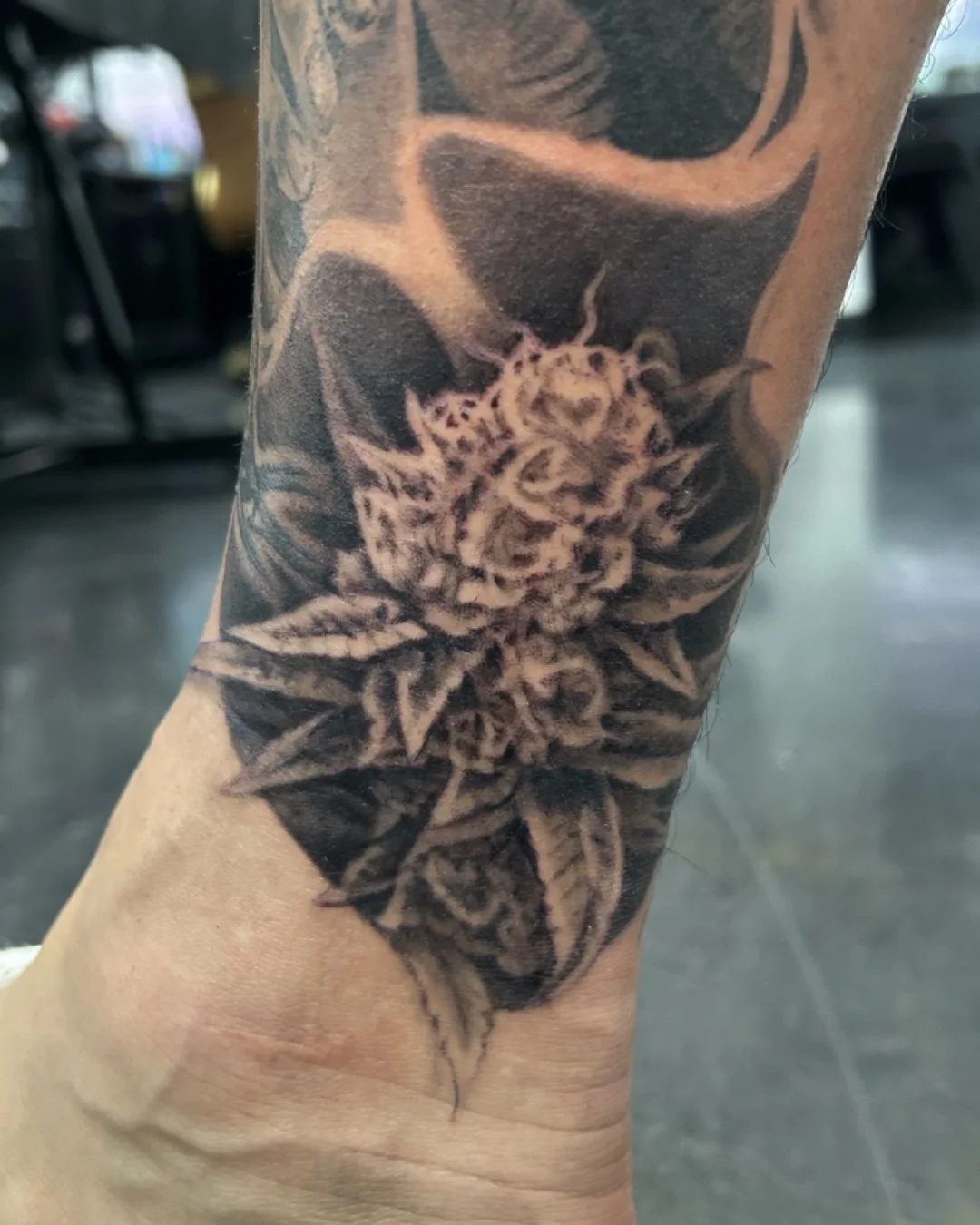 Close-up of a black-and-gray floral tattoo featuring a detailed sunflower on a person's forearm.