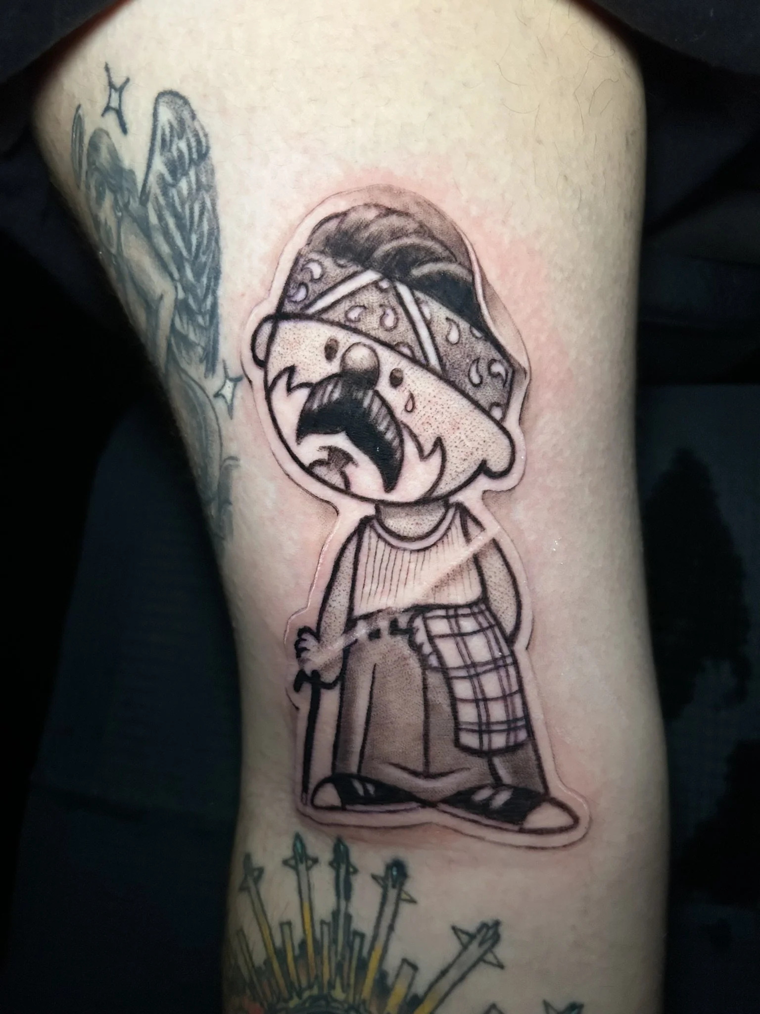 Detailed tattoo of a cartoon gnome wearing a patched pointed hat, sweater, pants, and shoes, surrounded by other tattoos on a leg.