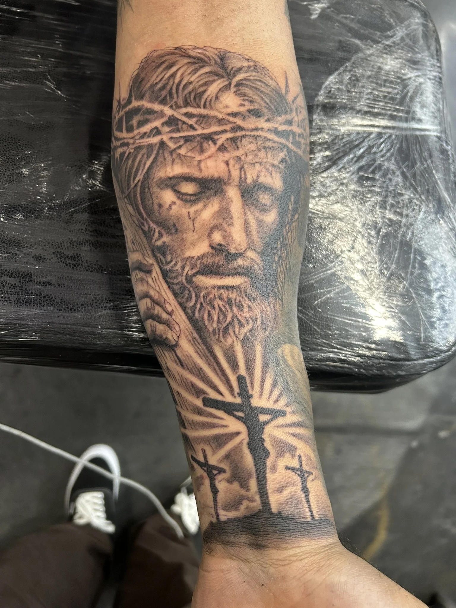 Close-up of a forearm tattoo featuring Jesus wearing a crown of thorns and a cross with radiant lines.