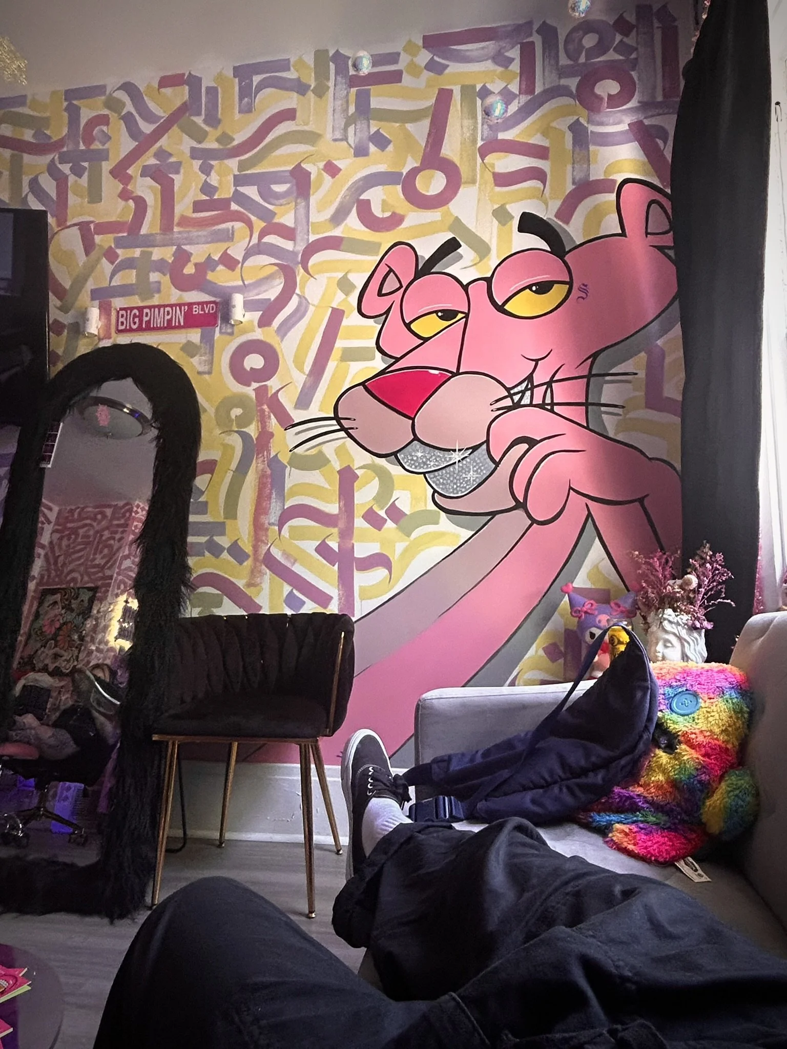 Colorful room featuring a large Pink Panther mural, abstract geometric wall art, a Big Pimpin' Boulevard sign, and rainbow furnishings.