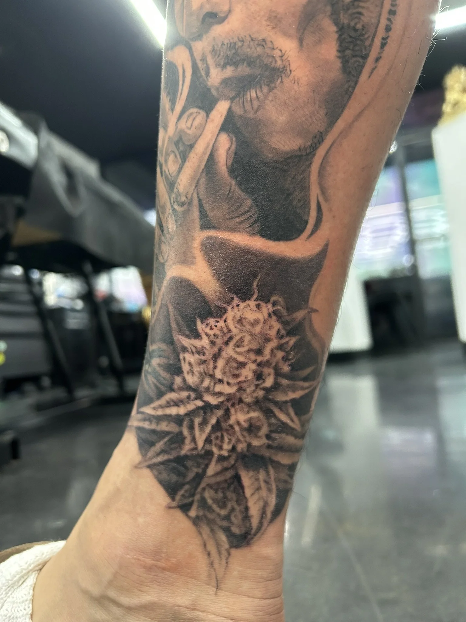 Close-up of a forearm featuring a detailed black-and-gray tattoo of a skull, flowers, and ornamental designs.