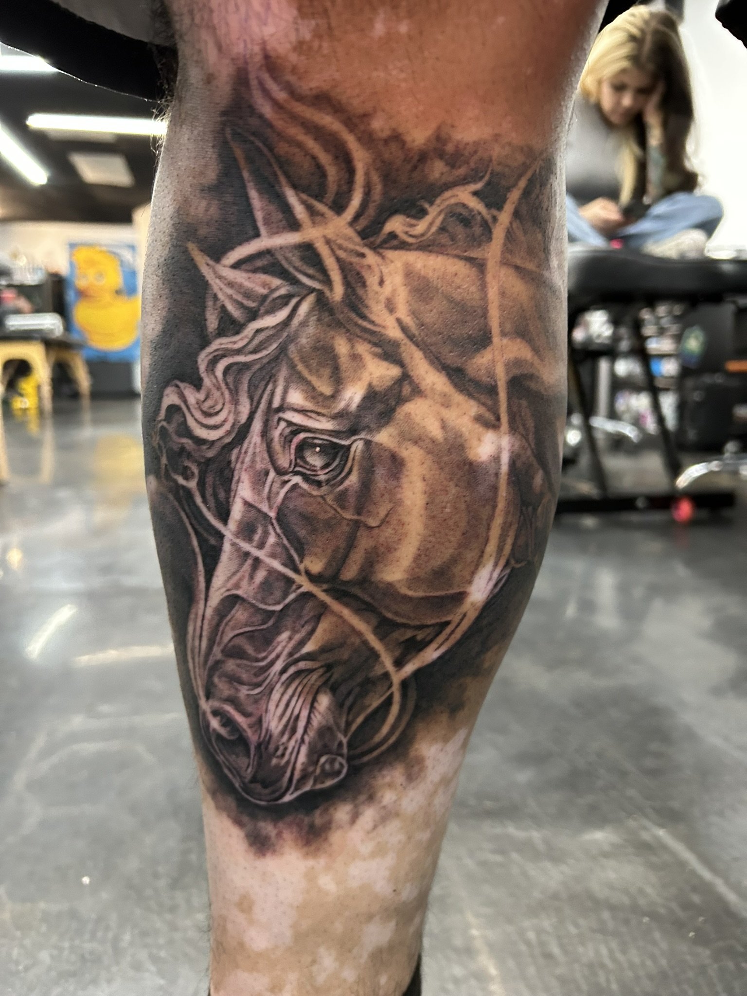 Close-up of a detailed black-and-gray tattoo featuring a horned skull and dragon-like creature on a person’s leg.