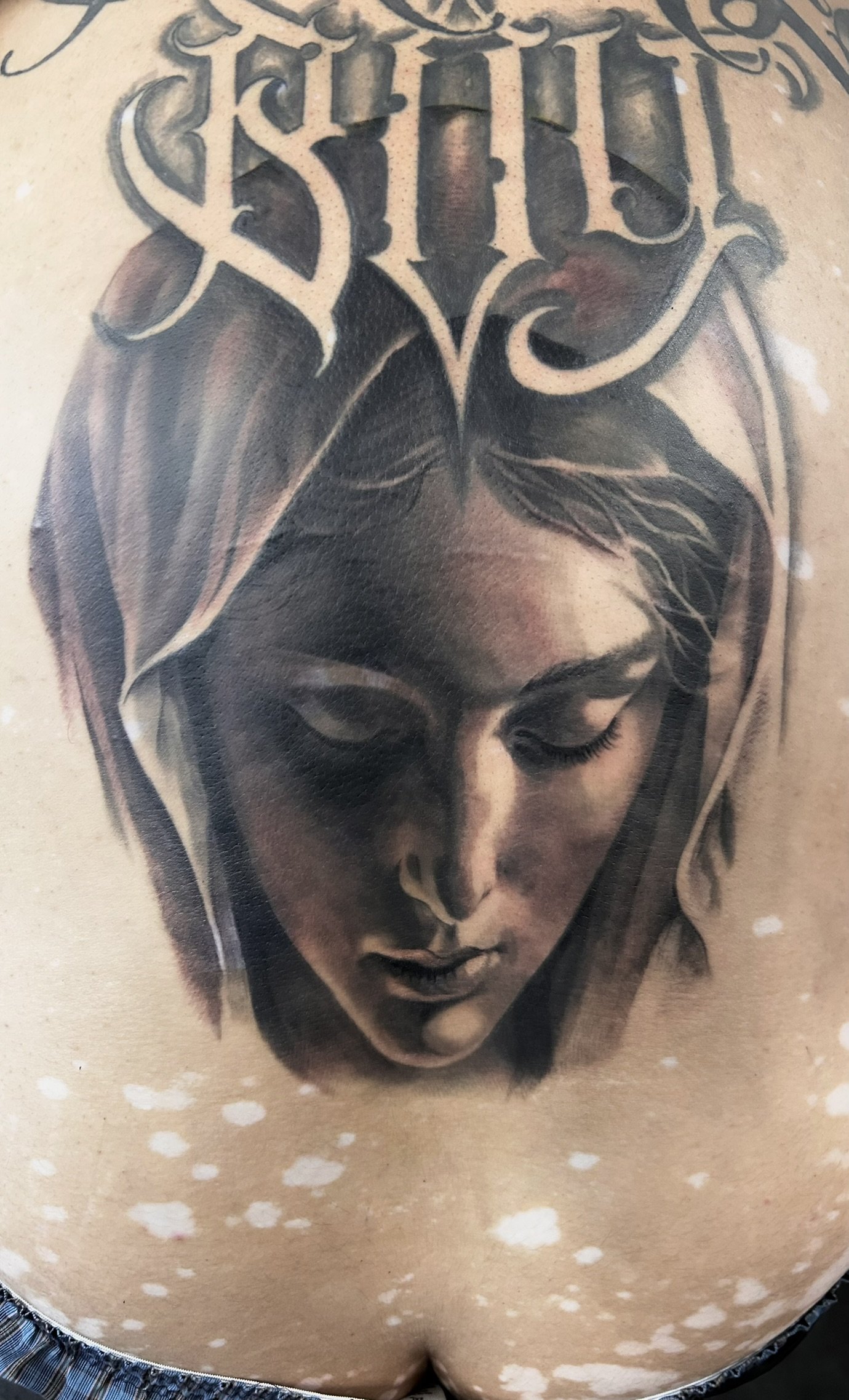 Detailed tattoo of a veiled woman with closed eyes and ornate lettering above her face