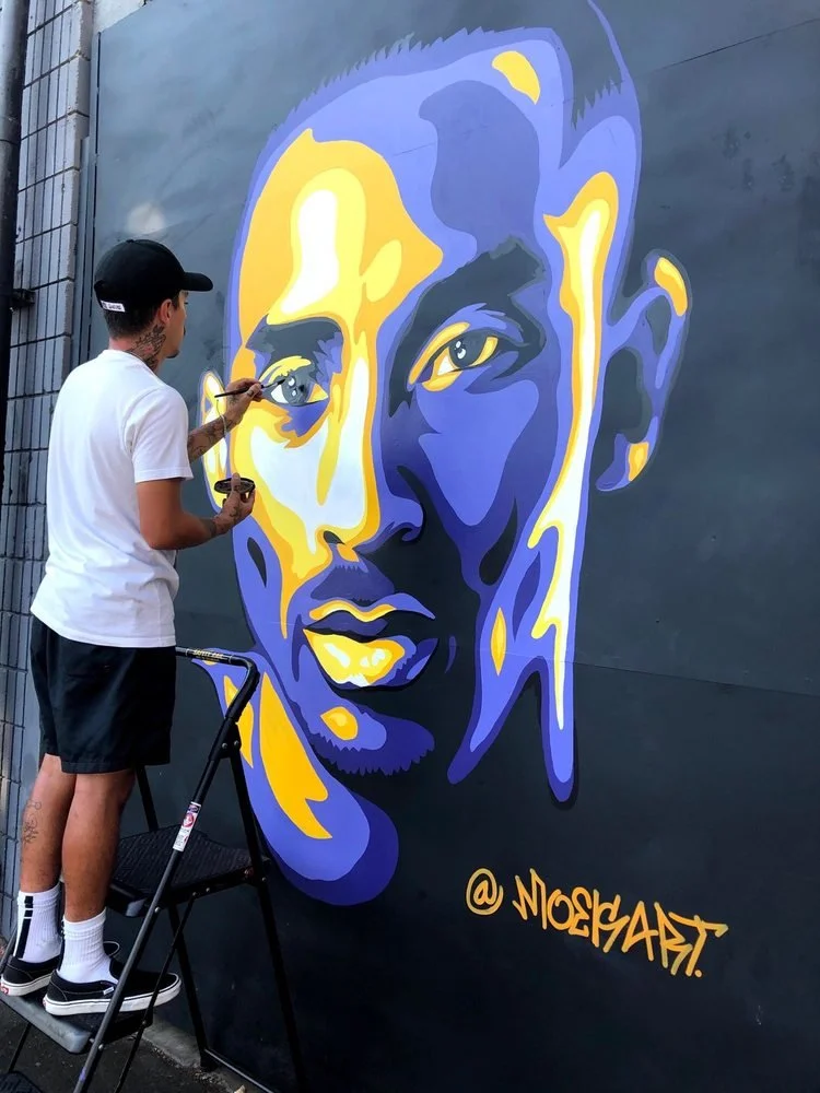 Artist painting a colorful blue, yellow, and purple portrait mural on a wall