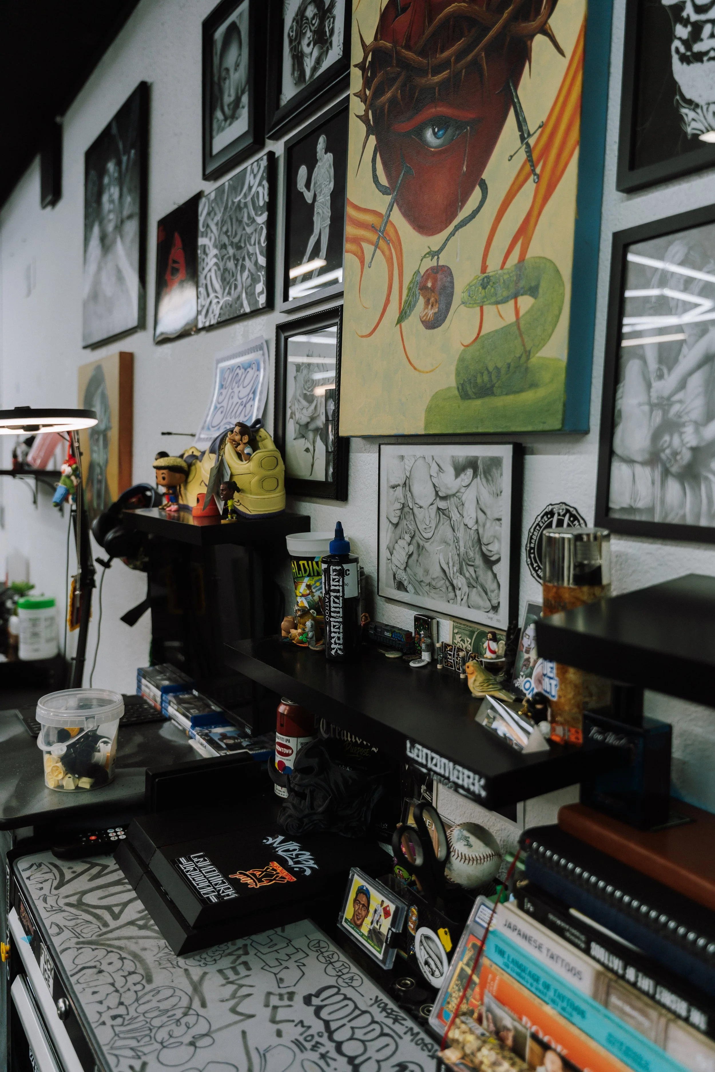 Eclectic art studio filled with framed artwork, a colorful thorn-crowned portrait, collectibles, art supplies, and graffiti-covered surfaces