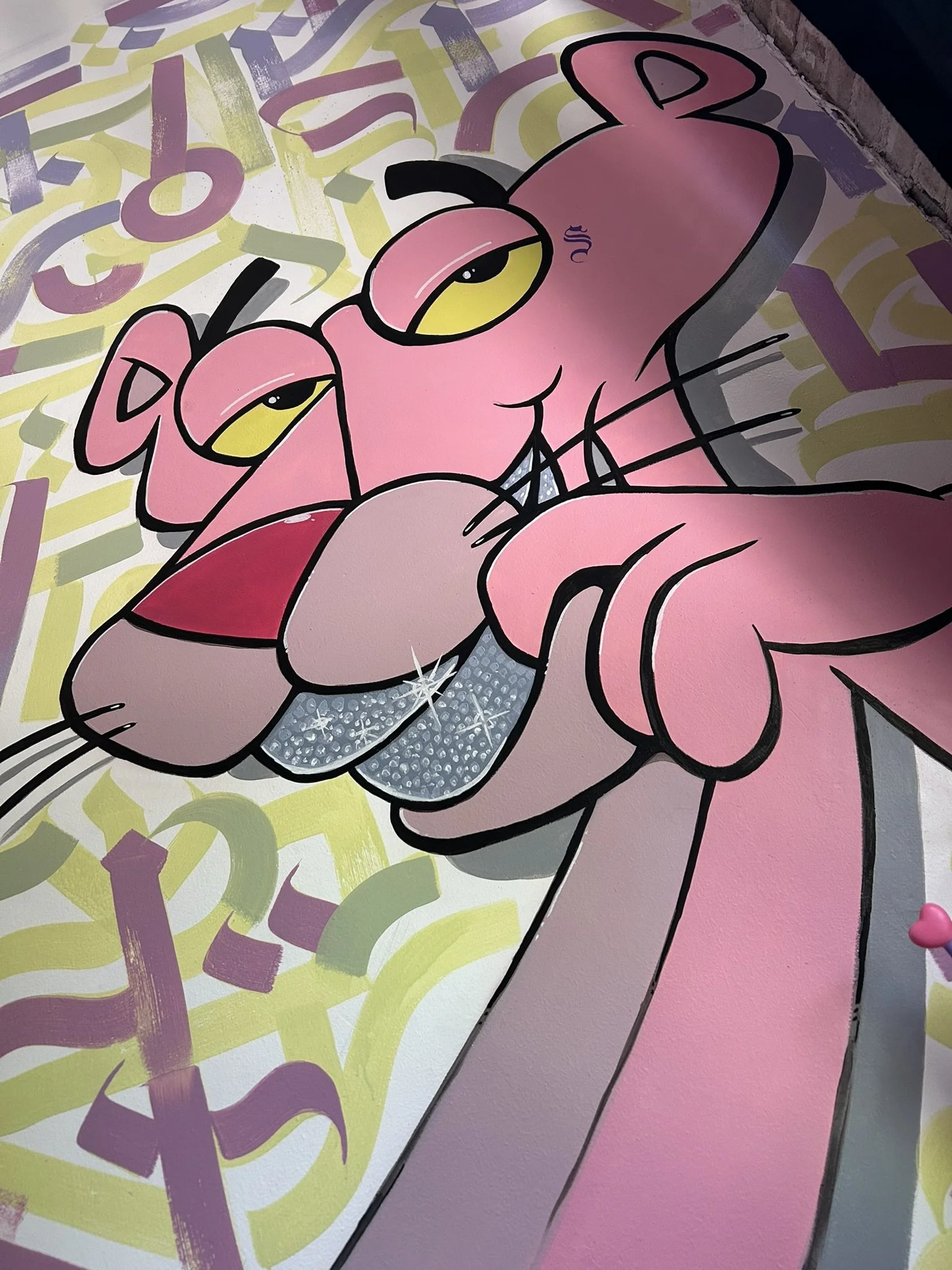 Colorful graffiti mural of a stylized pink panther with yellow eyes, black outlines, and a patterned pastel background.
