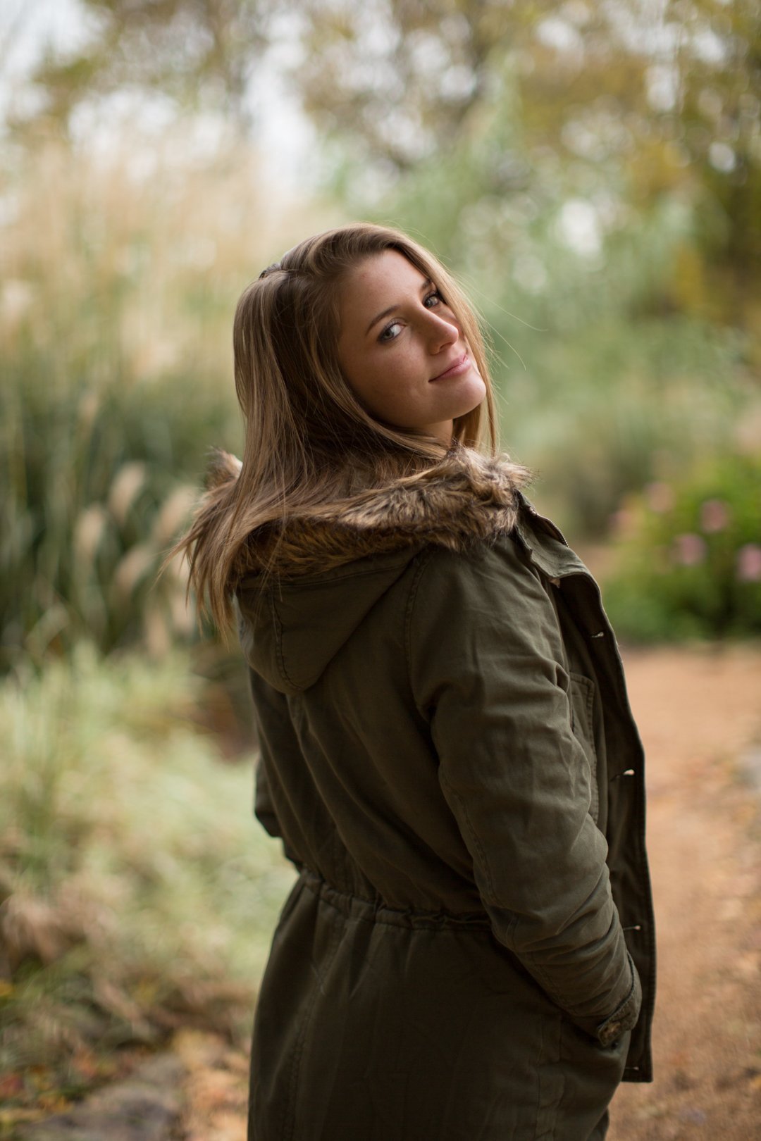 Portrait in an olive jacket on a garden path, with the surroundings visible.