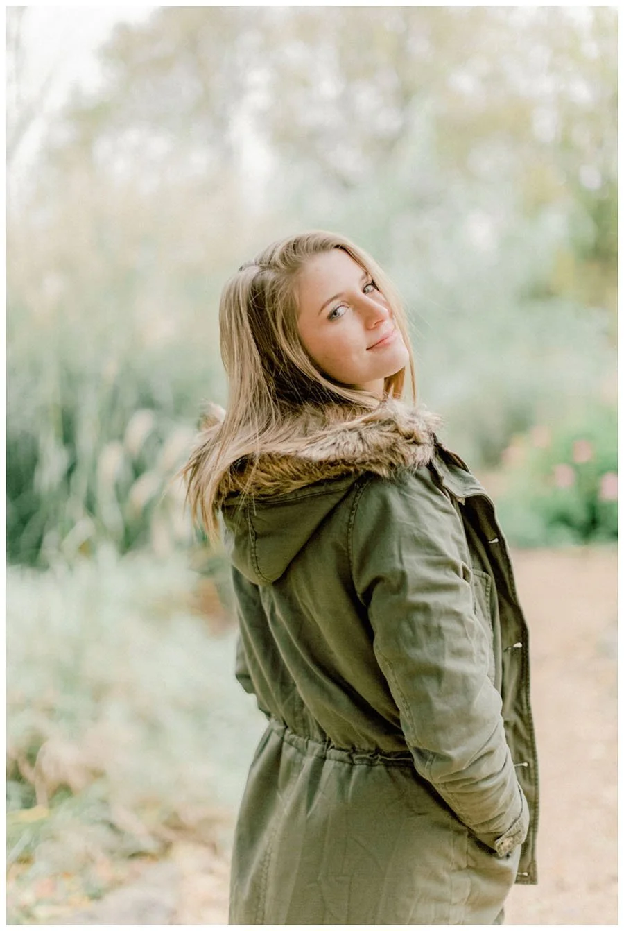 Edited portrait in an olive jacket on a garden path, with a softly blurred background.