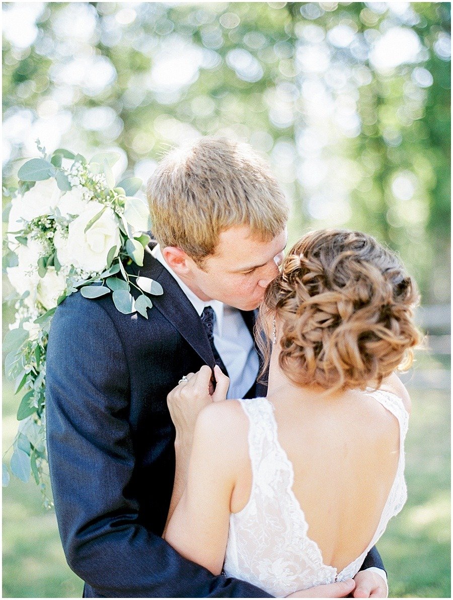 A groom kisses the bride’s cheek while they hold each other.