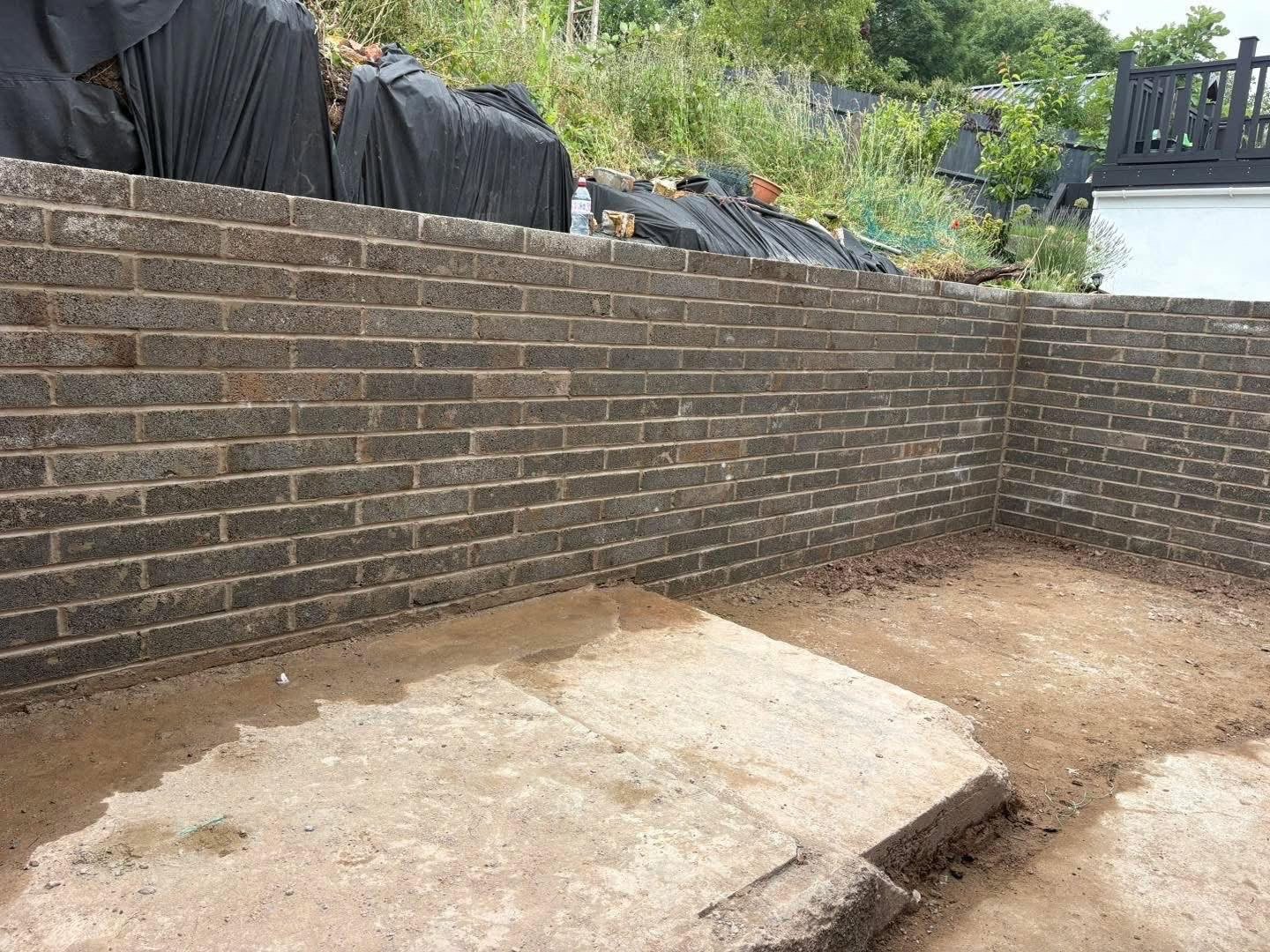 Newly built brick retaining wall surrounding a partially paved backyard patio