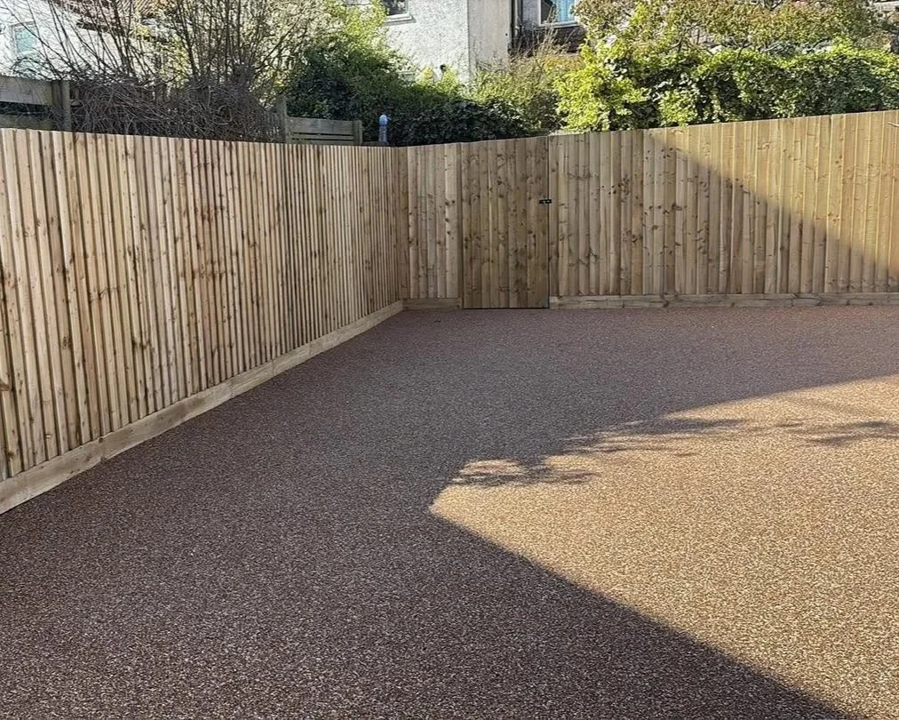 Enclosed residential driveway with a new wooden privacy fence and gravel surface