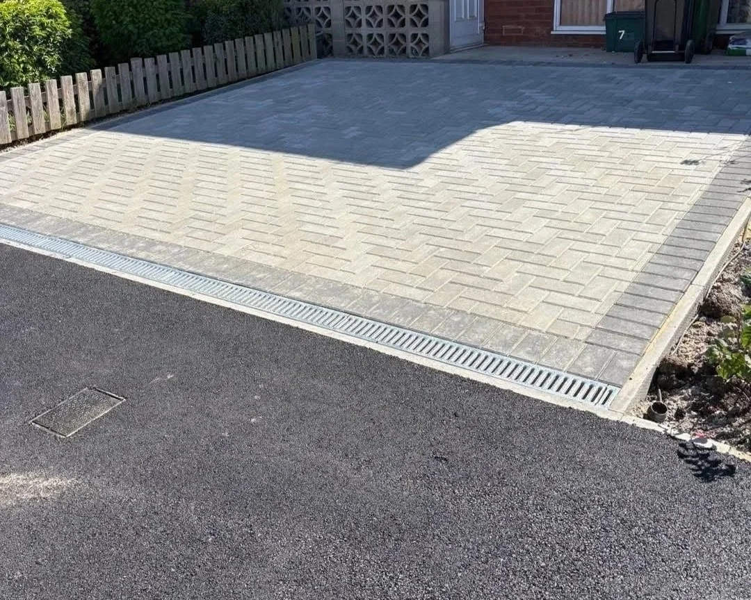 Newly paved brick driveway with a linear drainage grate beside a residential street