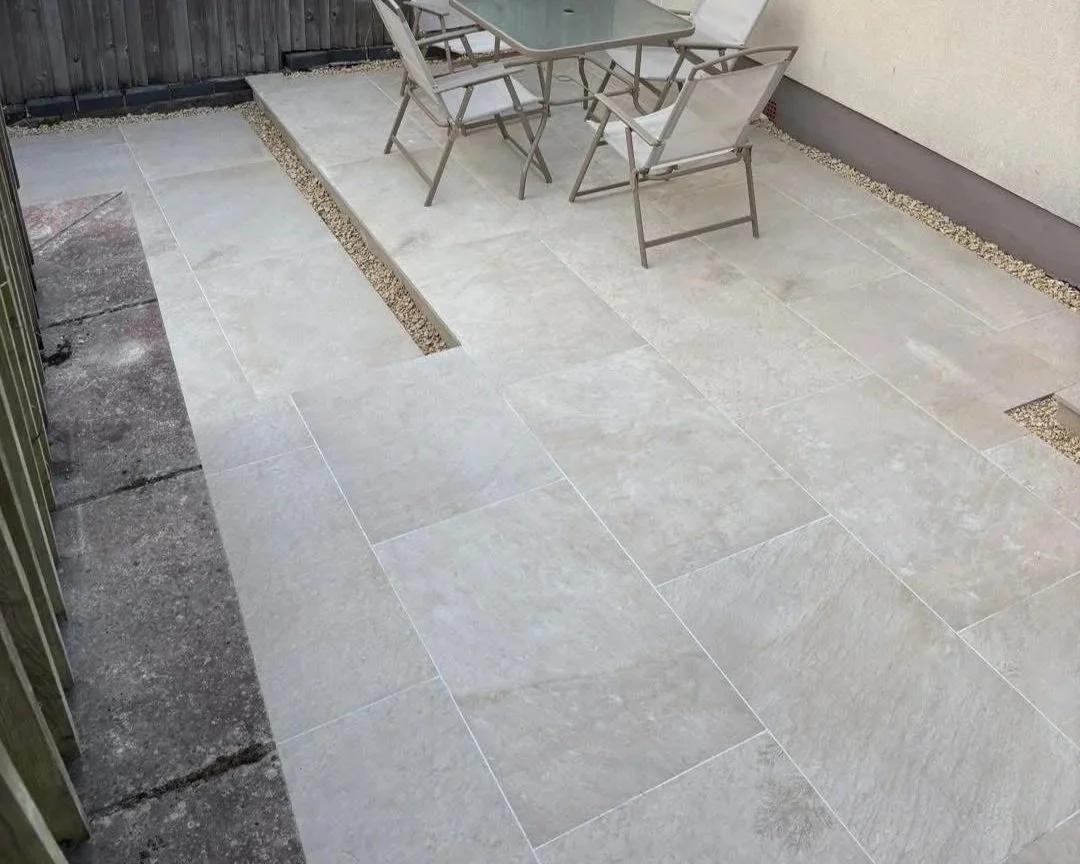 Outdoor patio with large light-gray tiled flooring, gravel borders, and a glass-top table with folding chairs
