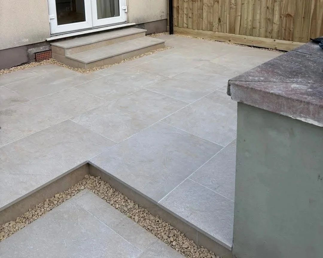 Gray tiled patio with steps to white double doors, gravel borders, and a wooden fence
