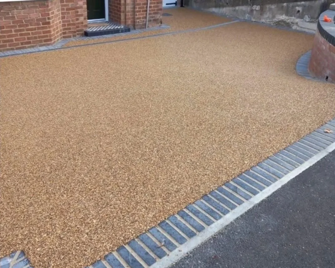 Resin-bound gravel driveway and walkway bordered by brick paving beside a brick building.