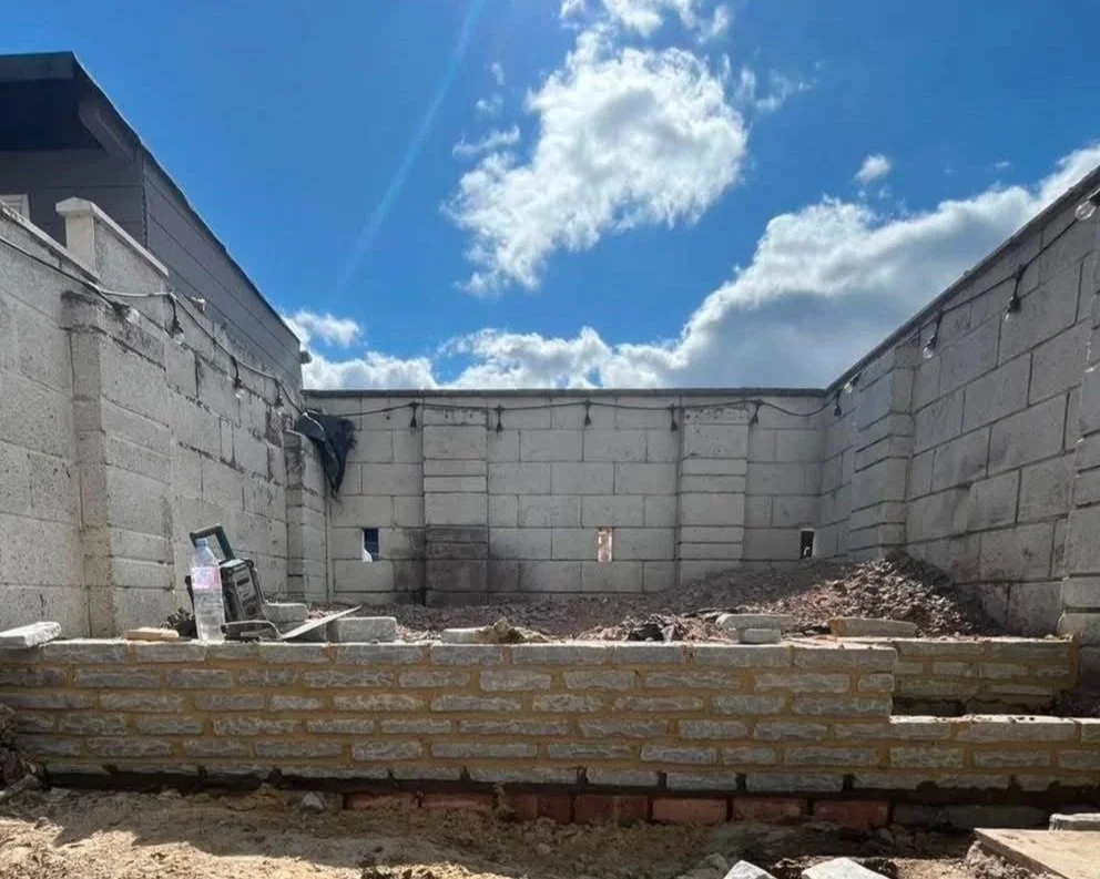 Partially constructed cinder block building with exposed brick foundation under a bright blue sky