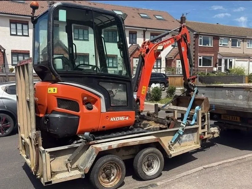 Kubota mini excavator secured on a dual-axle trailer parked on a residential street