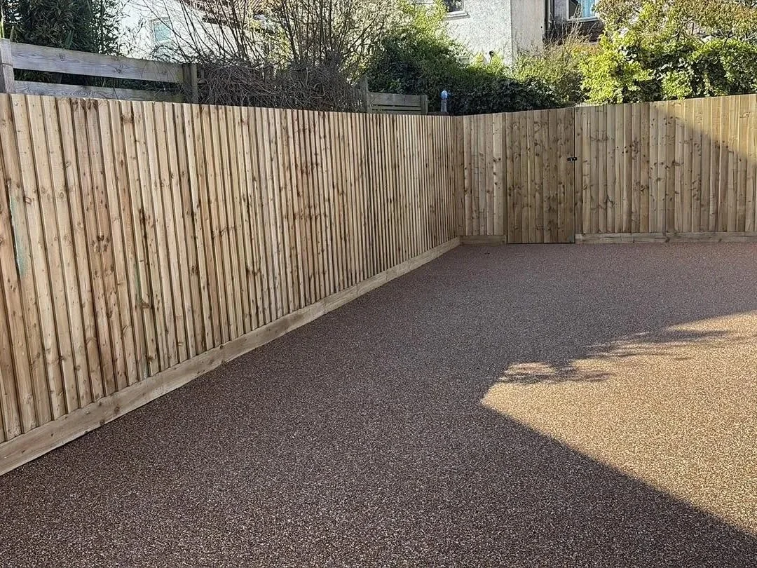 New wooden privacy fence enclosing a freshly surfaced gravel driveway or patio beside a house