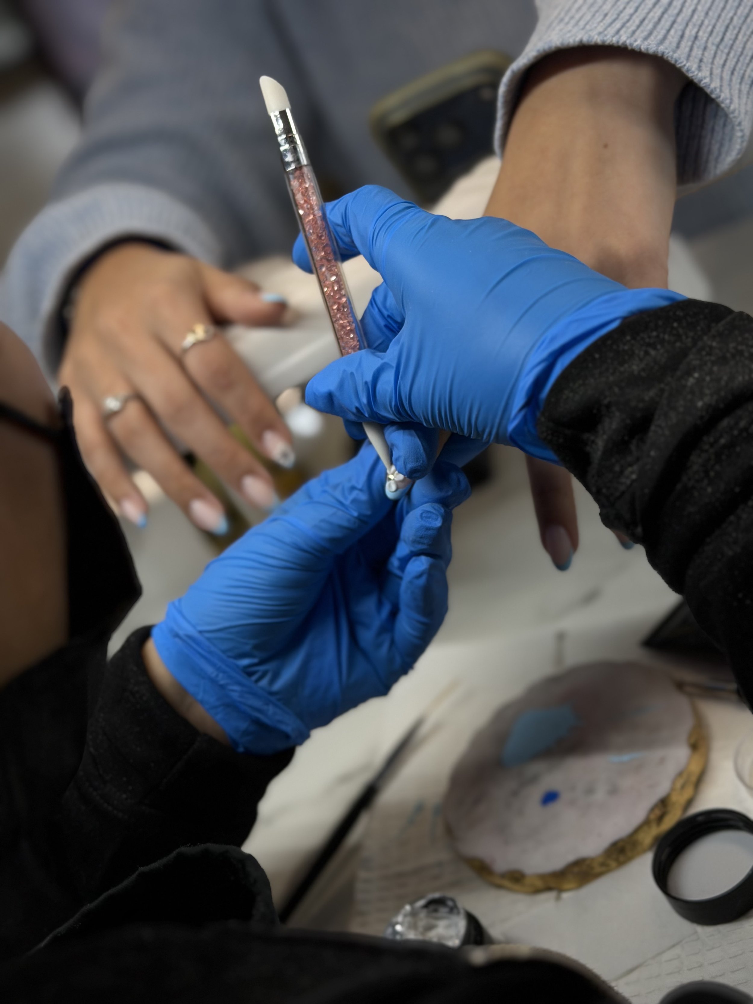 Nail tech wearing blue gloves adding gems to nails