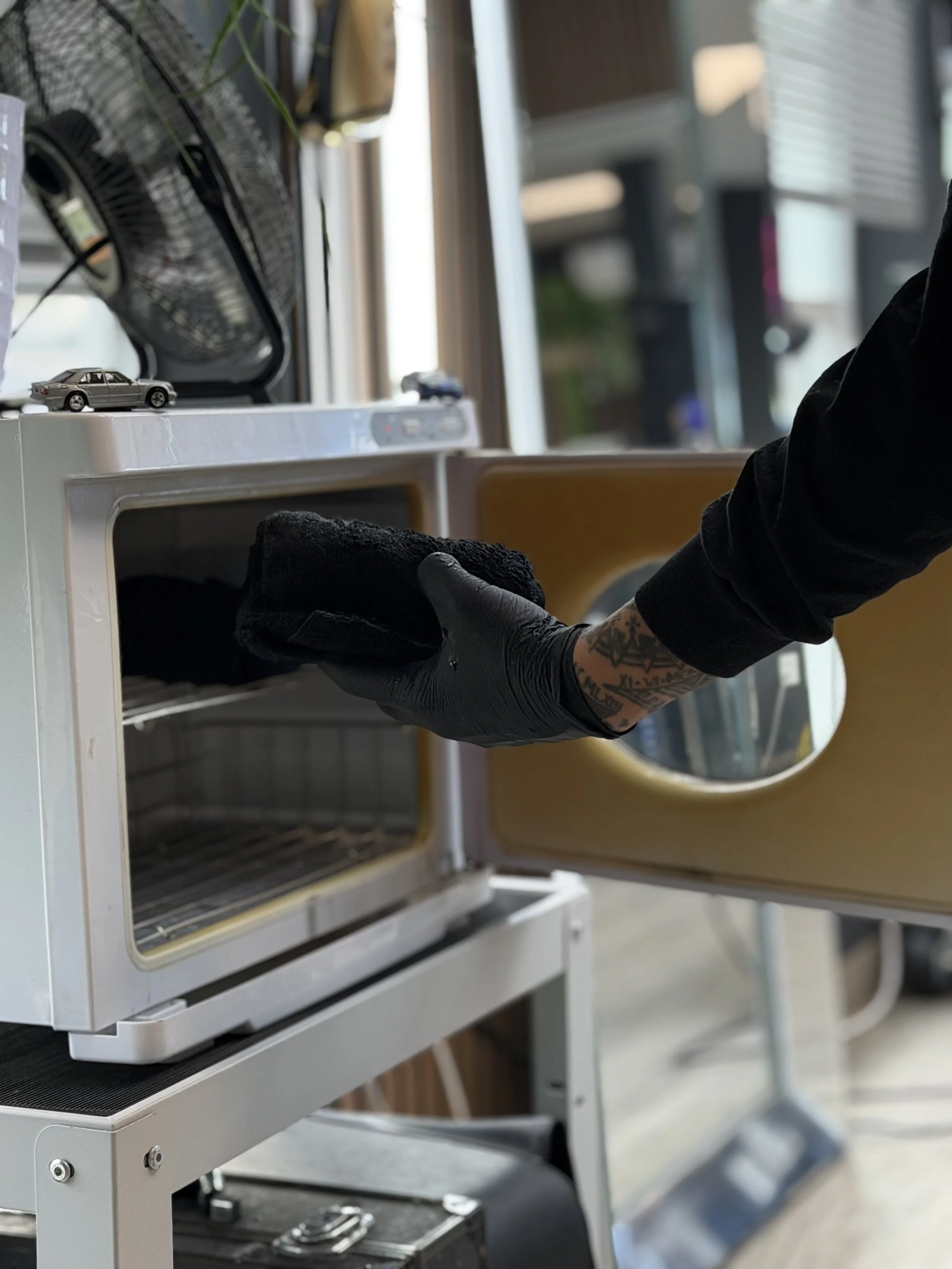Barber removing hot towel from warmer wearing black gloves for a straight razor shave