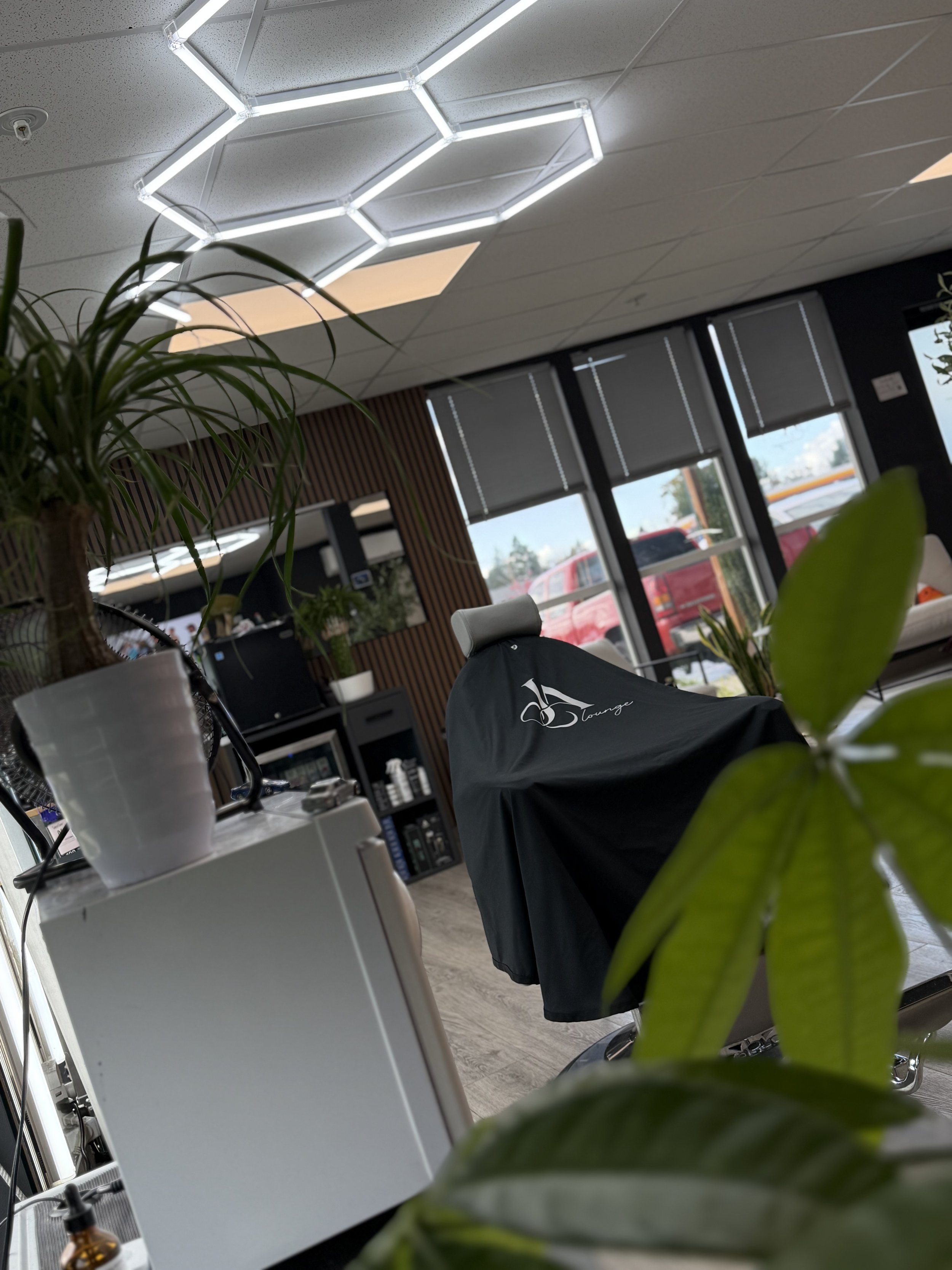 Modern hair salon interior with geometric LED ceiling lights, styling chairs, mirrors, large windows, and potted plants.