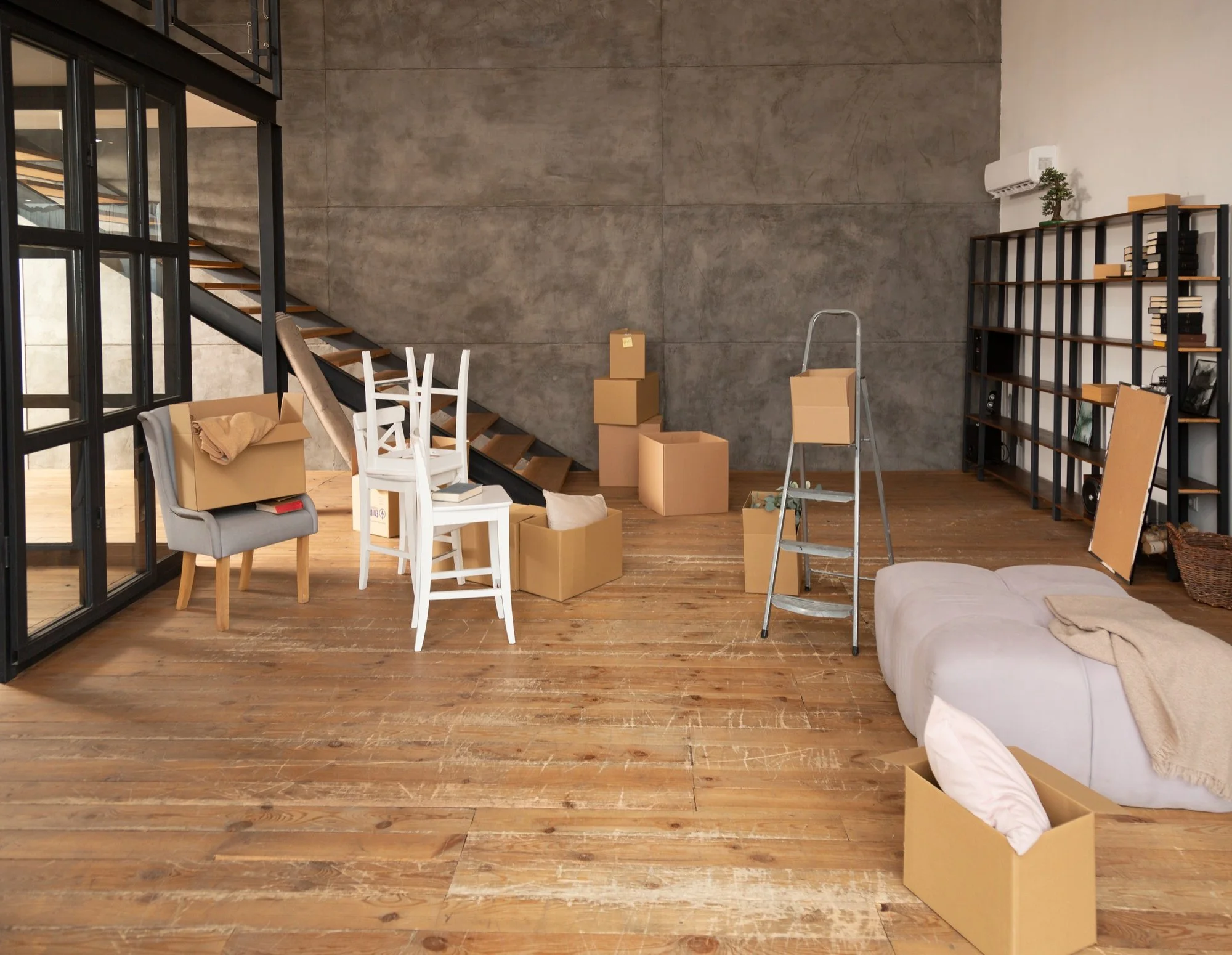 Modern loft interior with moving boxes, a step ladder, stacked chairs, wooden staircase, and bookshelves