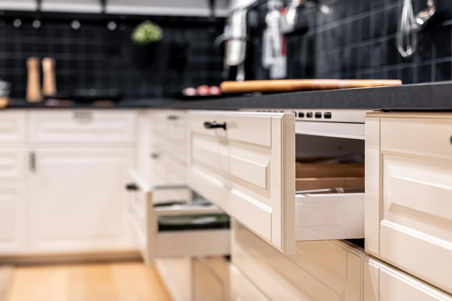 Modern kitchen with open white cabinets, drawers, black countertops, and wood-handled utensils
