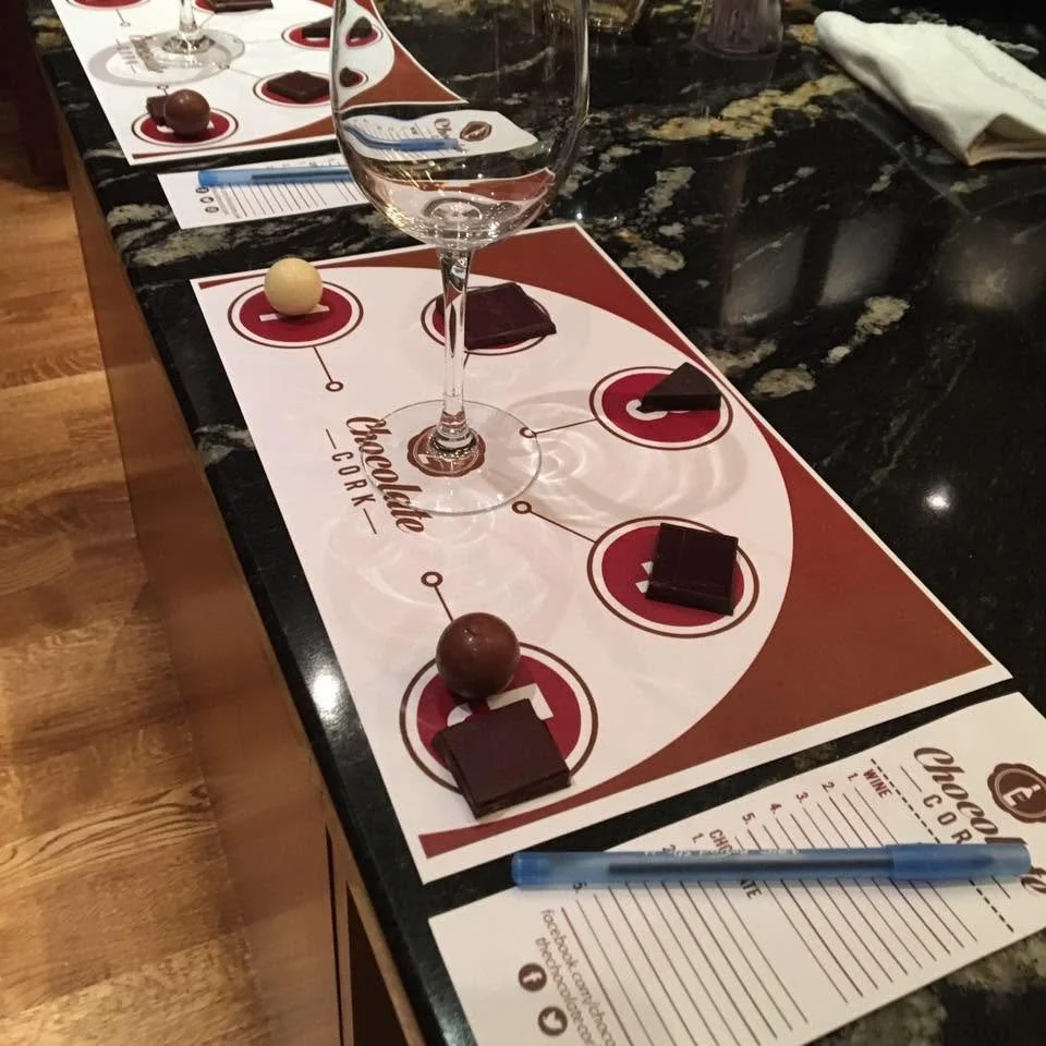 A Chocolate Cork tasting place setting with chocolates, wine glasses and pairing notes.