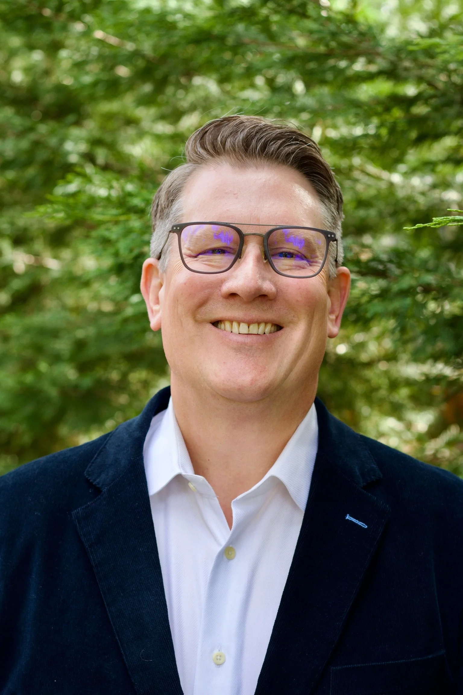 Troy S. Anderson, church and nonprofit lawyer, smiling and wearing glasses and a dark blazer outdoors against a leafy green background