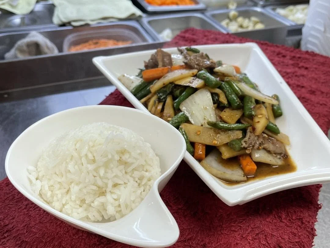 Bowl of white rice with a plate of saucy mixed vegetables and beef stir-fry.