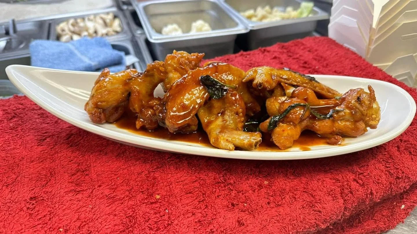 Plate of crispy chicken wings coated in glossy orange sauce and garnished with herbs at a restaurant kitchen counter