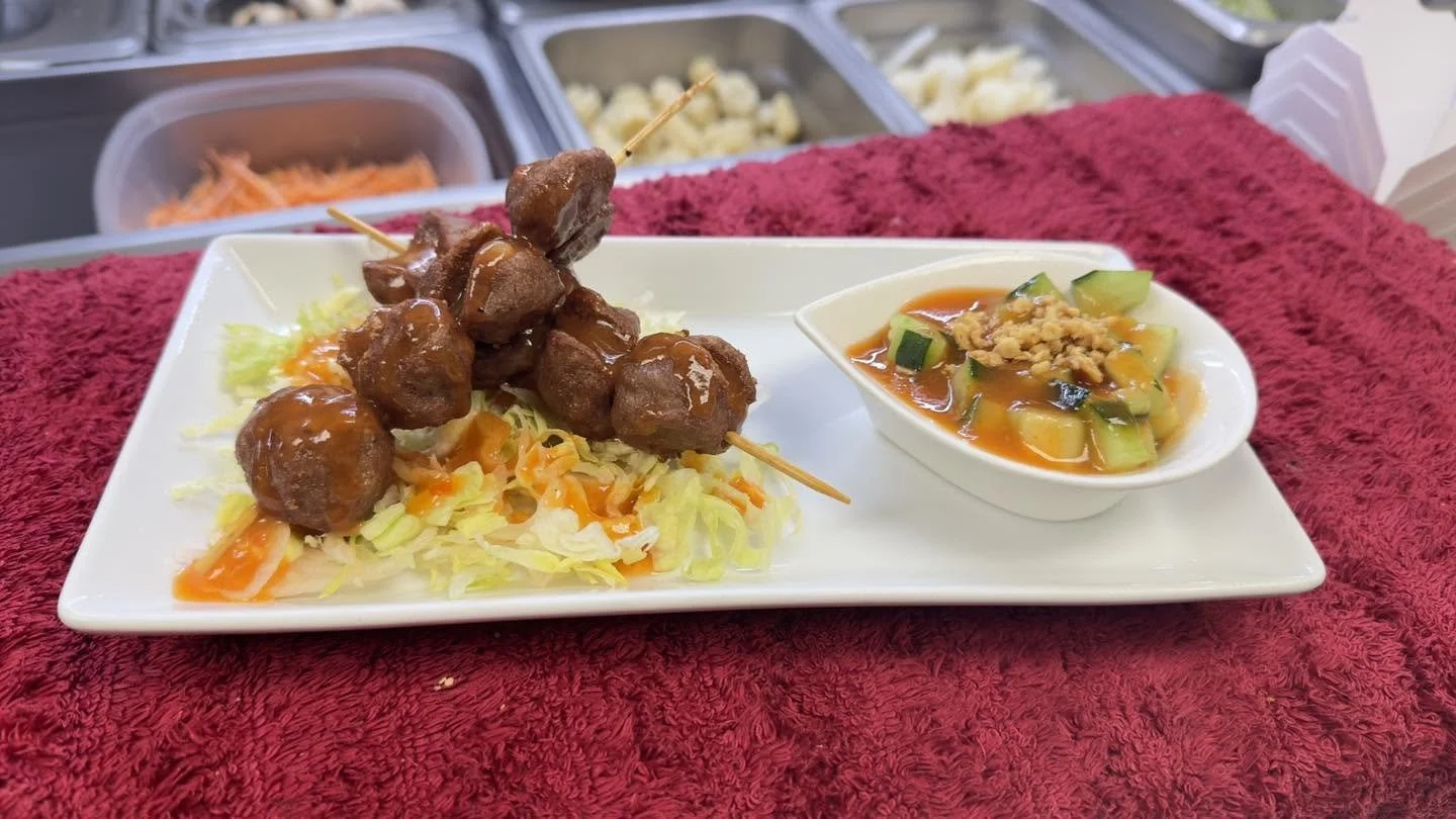 Skewered glazed meatballs served over shredded lettuce with a side of cucumber and orange dipping sauce