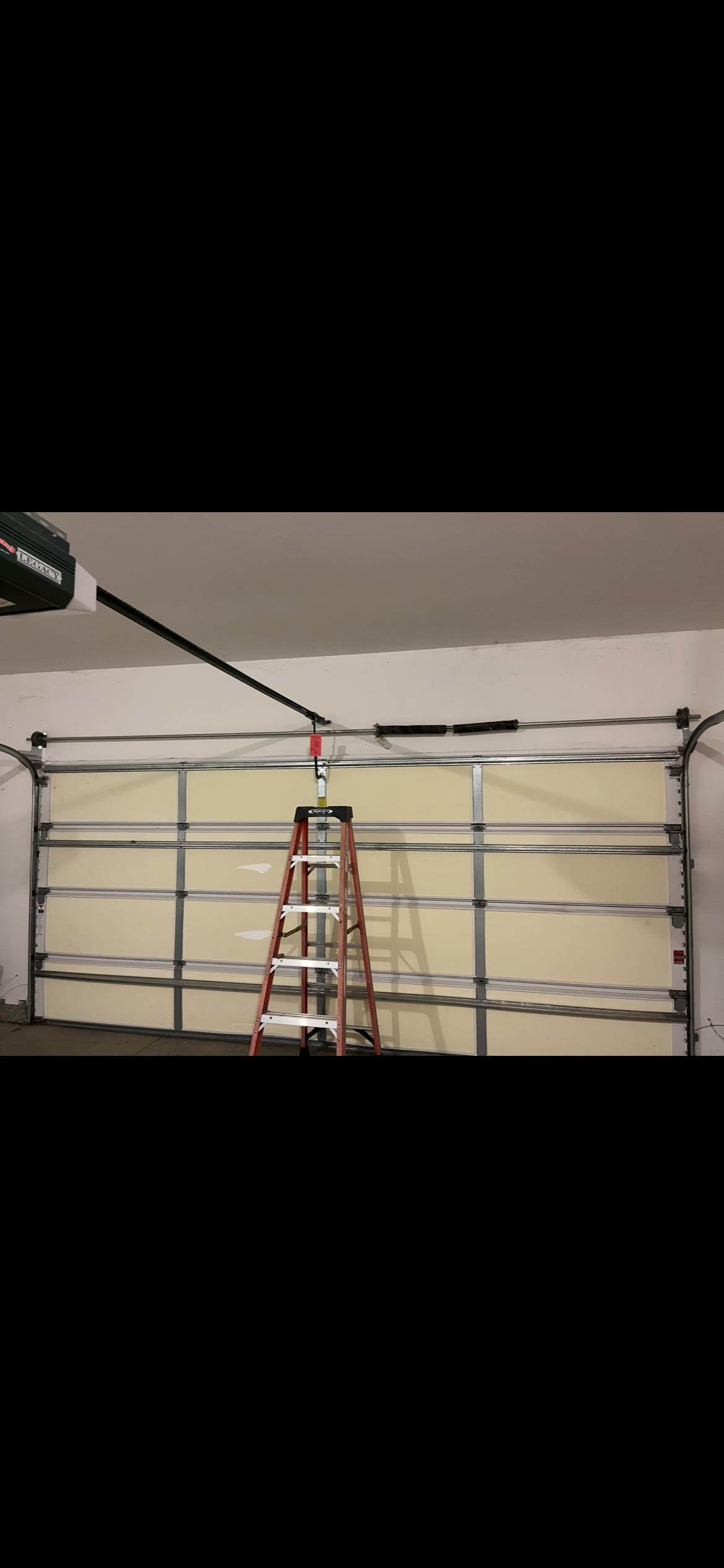 Red step ladder in front of a residential garage door with overhead door hardware