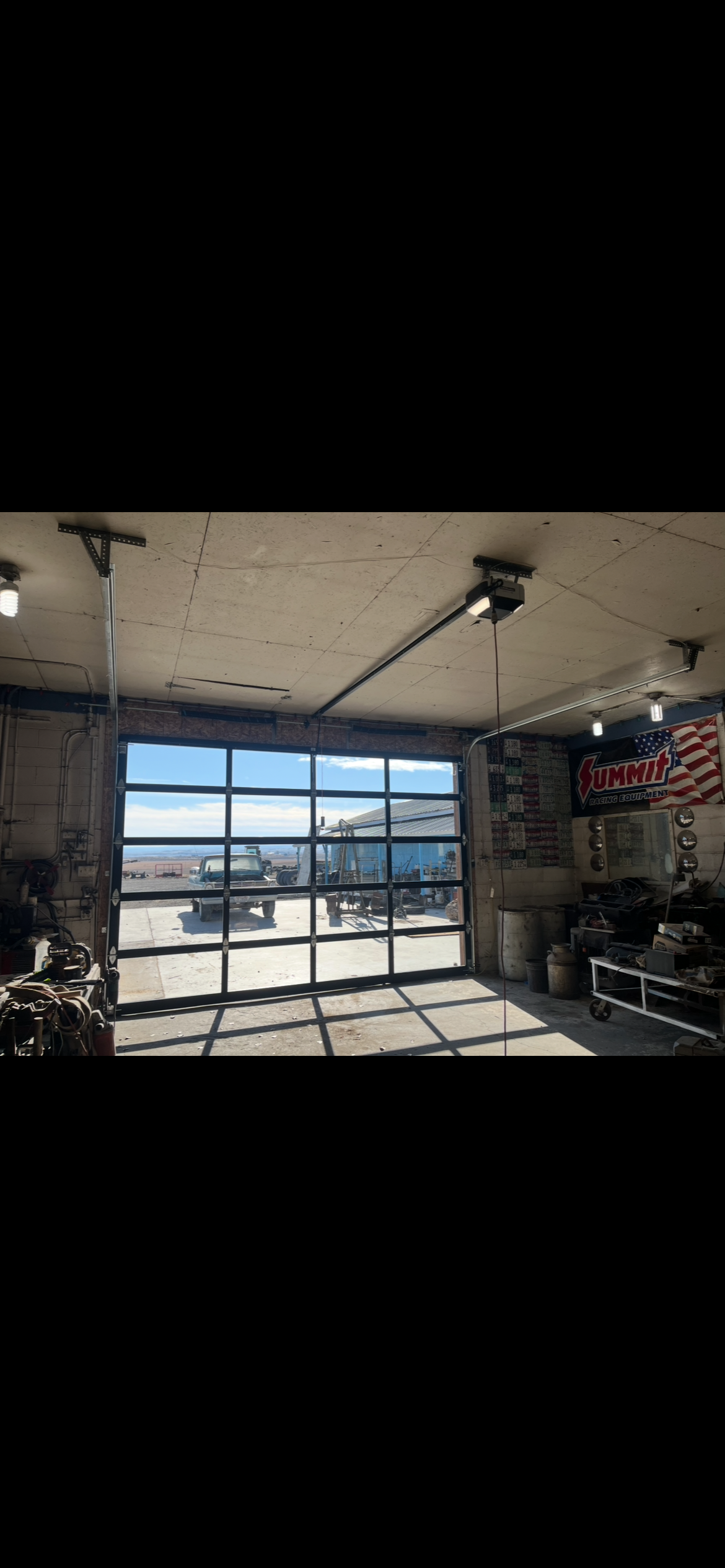 Automotive repair garage with an open glass-paneled door, vintage pickup truck outside, racing equipment, tools, and a Summit Racing Equipment banner.