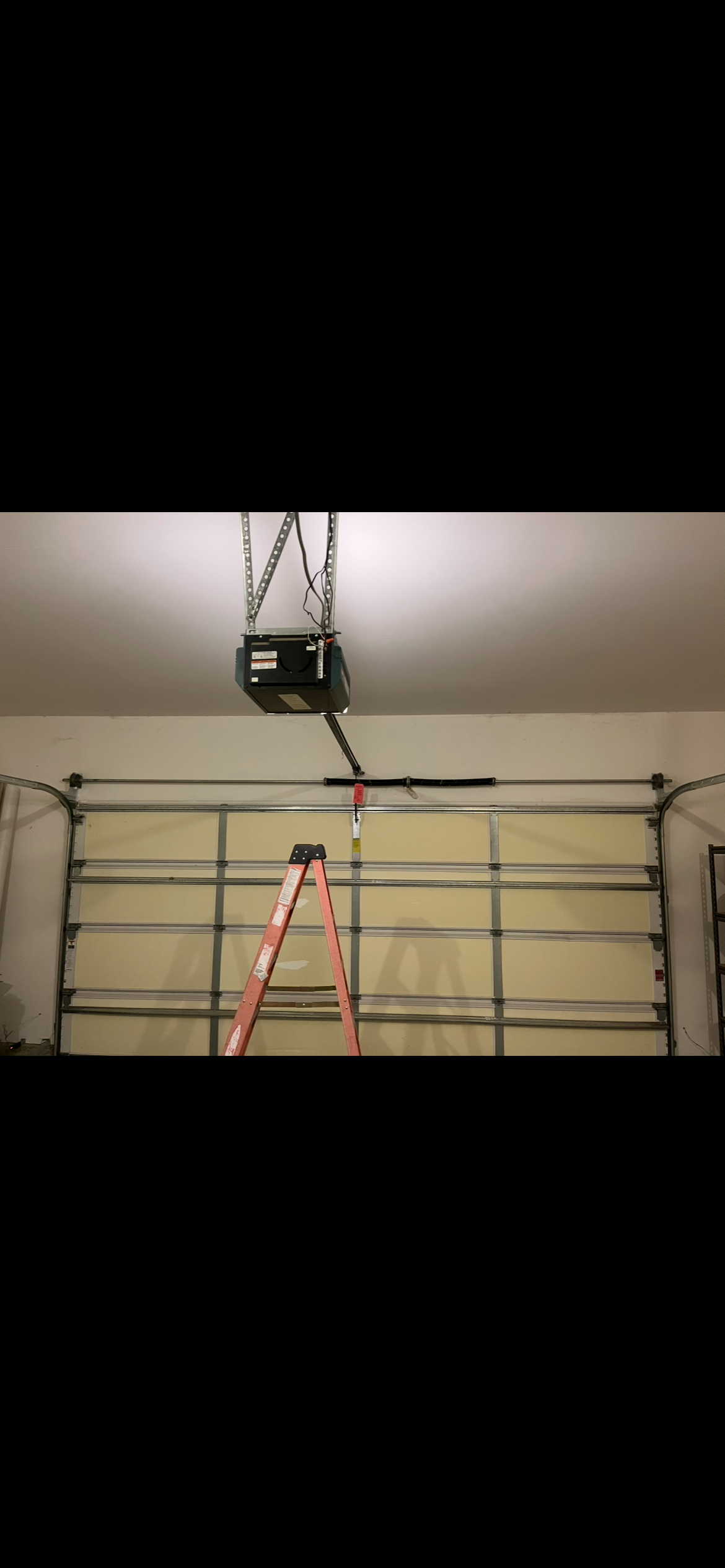 Garage door opener mounted above a sectional garage door, with an orange step ladder beneath it.