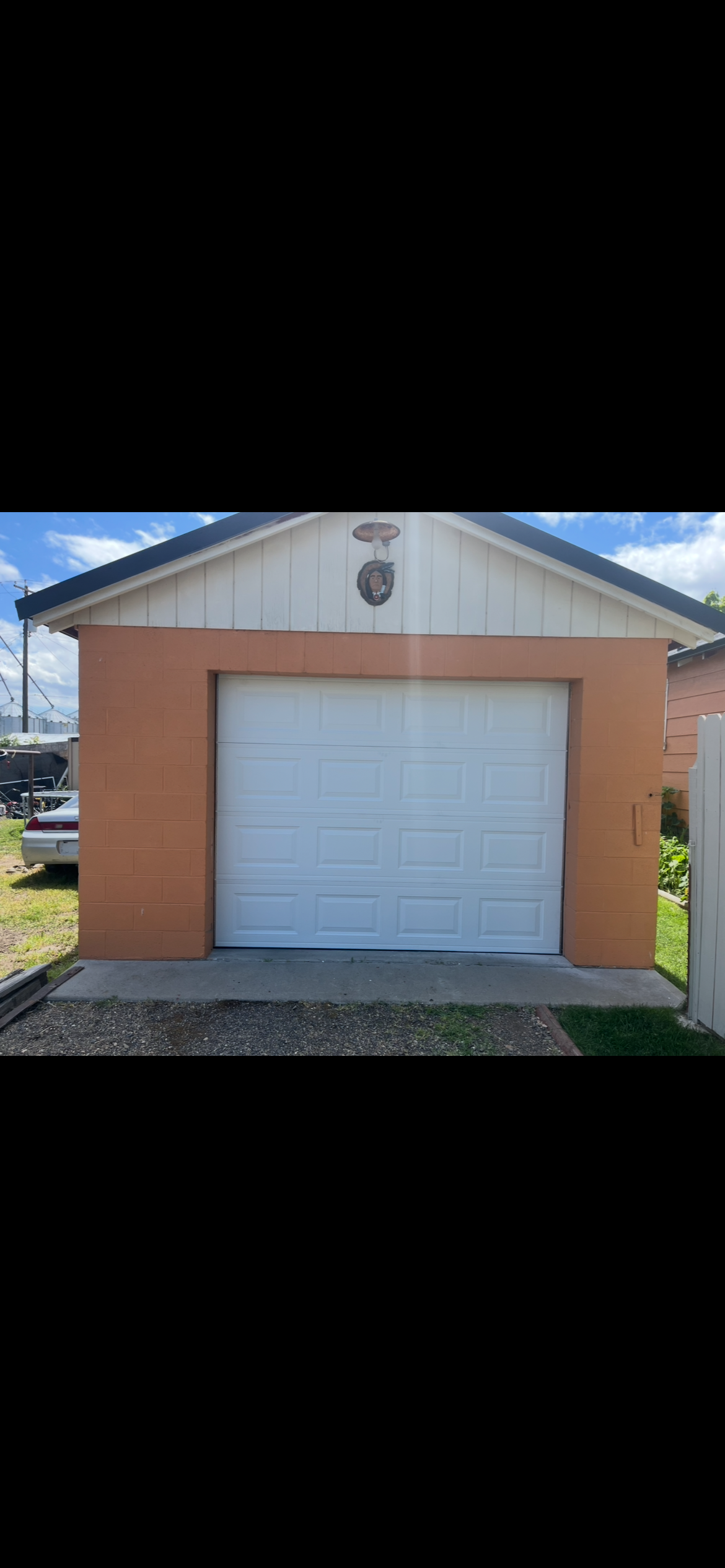 Small peach-colored detached garage with a white paneled overhead door and decorative Native American portrait beneath the gable.
