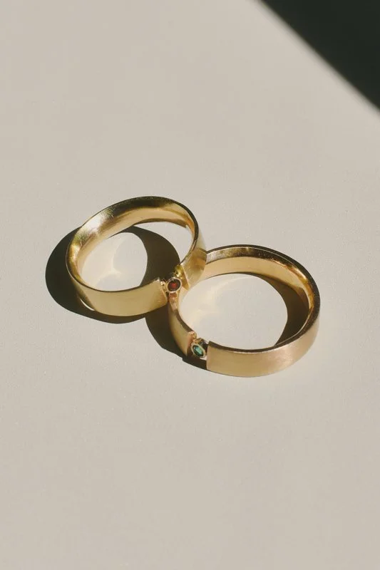 Pair of gold-toned hinged hoop earrings with small red and turquoise gemstones on a neutral background
