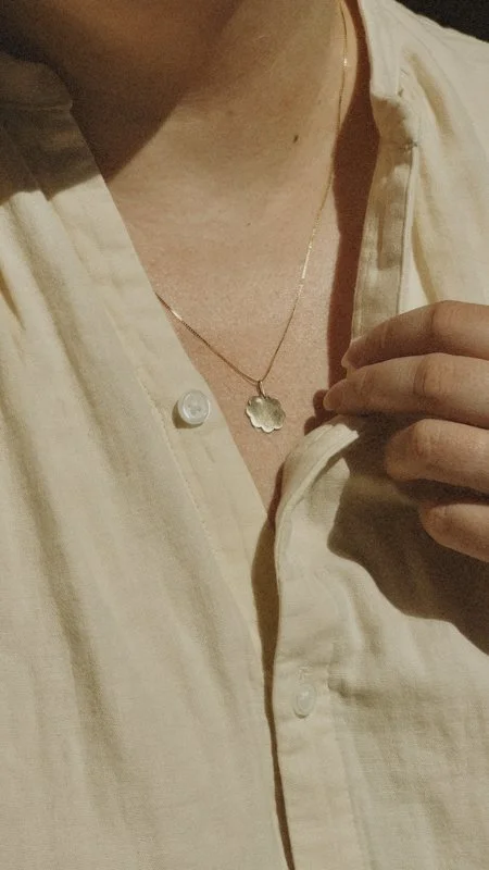 Close-up of a person wearing an open white shirt and delicate leaf-shaped pendant necklace
