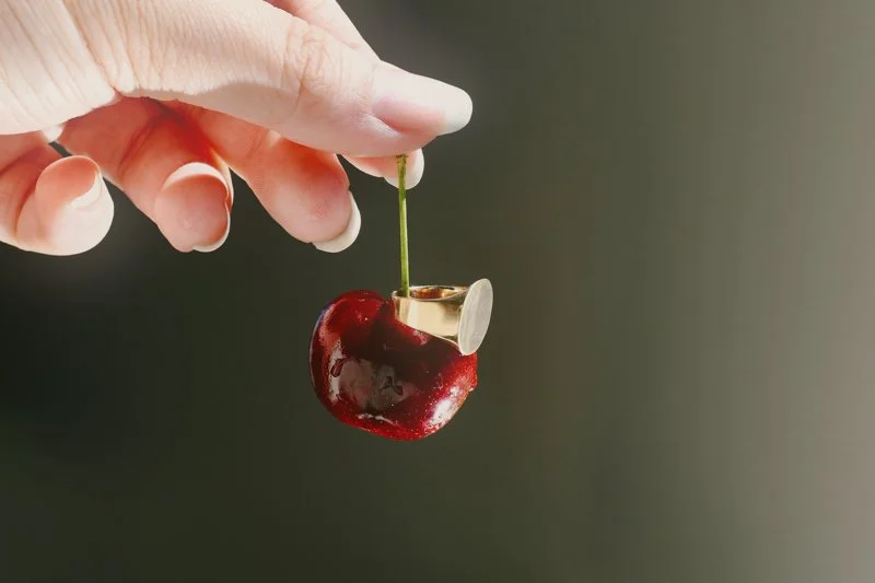 Hand holding a cherry with a bitten cigarette attached to its stem