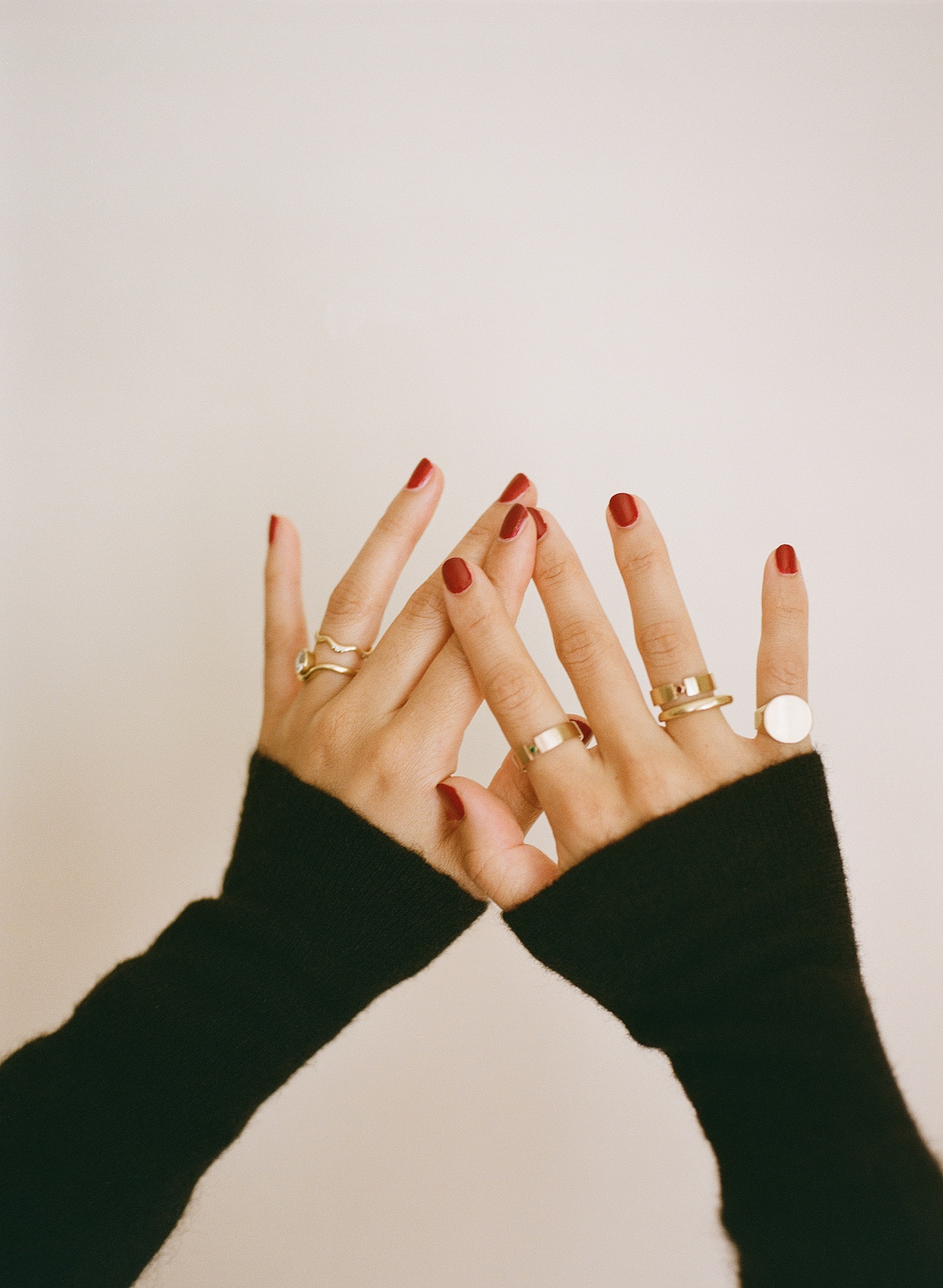 Close-up of hands with red manicured nails and multiple rings against a white background