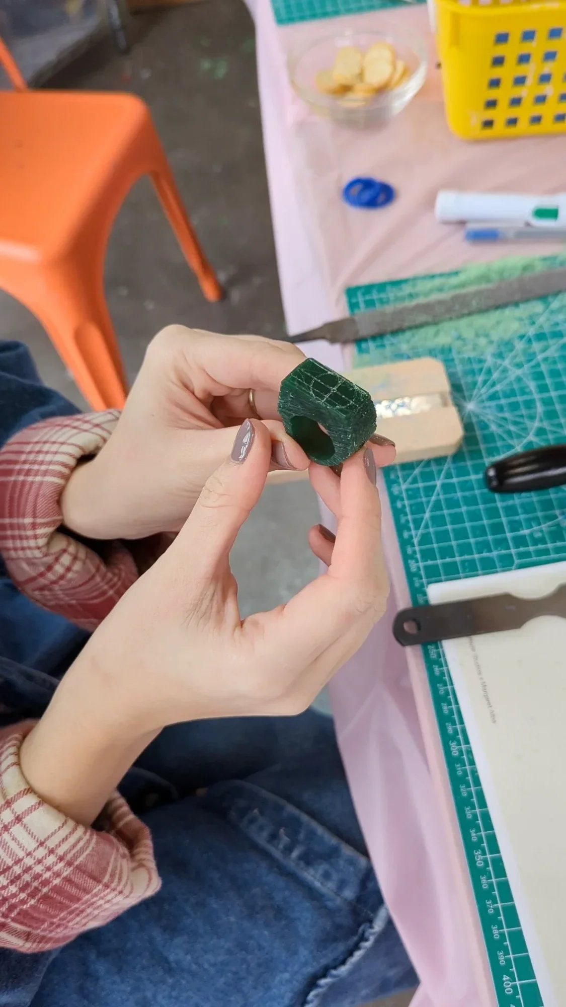 Person holding a textured green handmade ring beside a crafting mat and tools